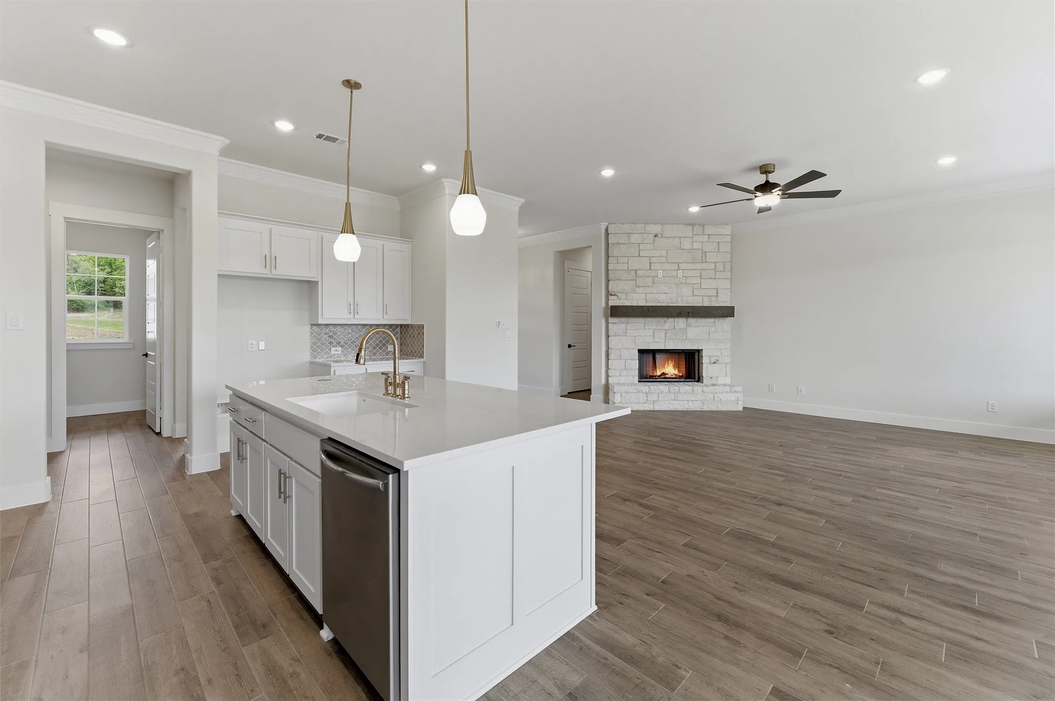 Open-concept living space featuring wood-finish flooring, a stone fireplace with wood mantel, and a ceiling fan