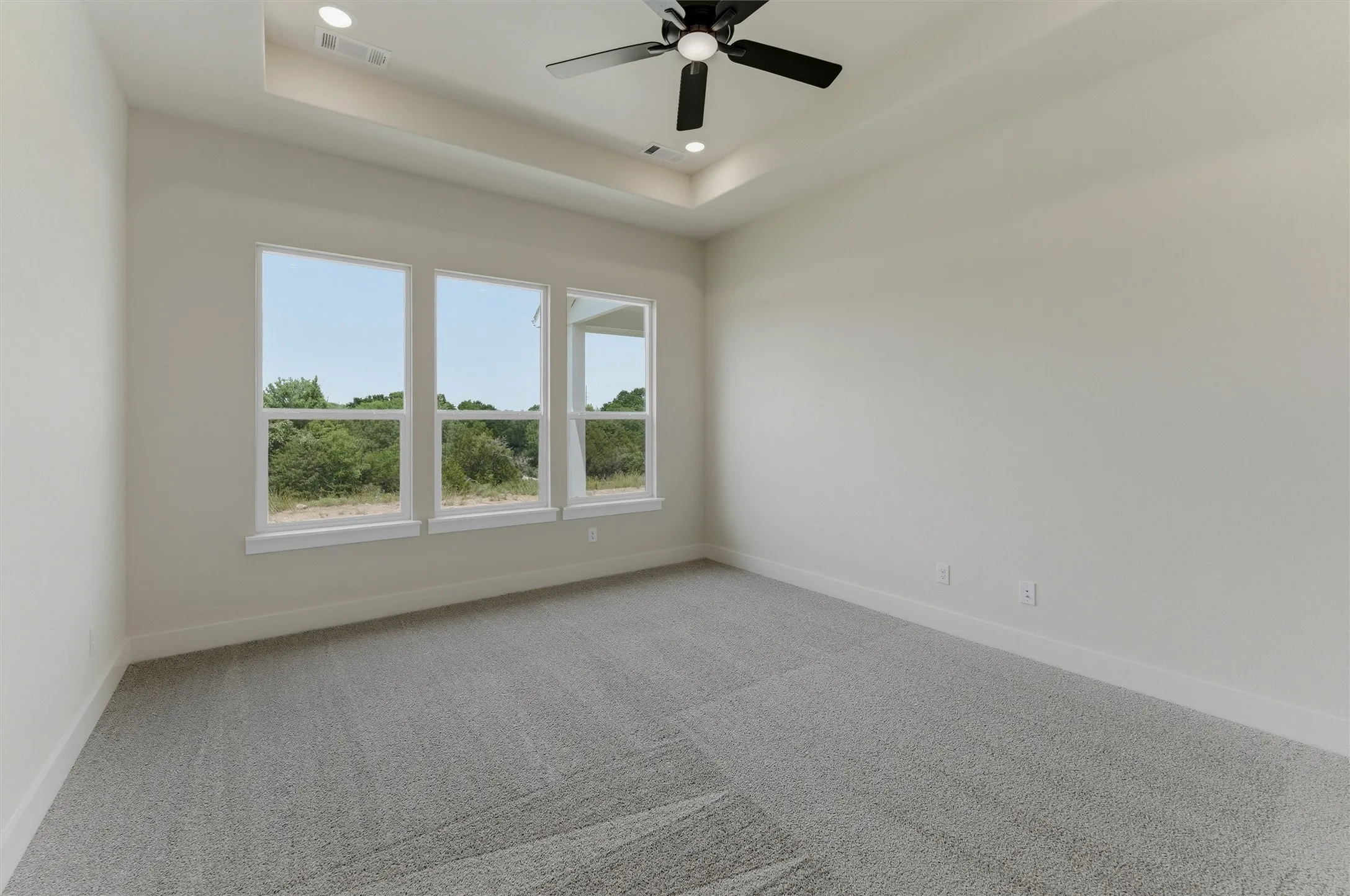 Room featuring three large windows, a tray ceiling with recessed lighting, a ceiling fan, and light grey carpeting