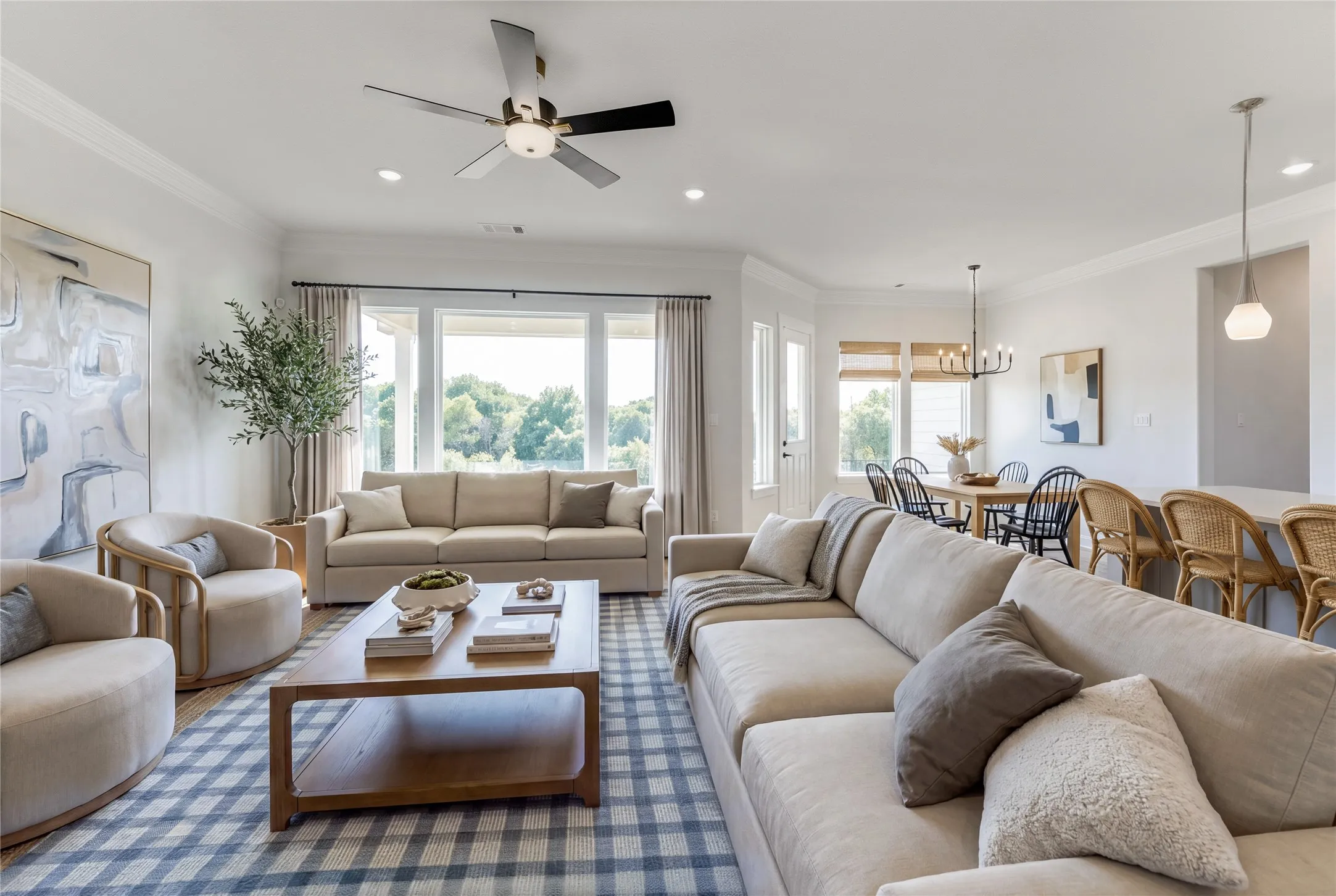 Open-concept living area featuring wood-finish flooring, abundant natural light from large windows, crown molding, and recessed lighting