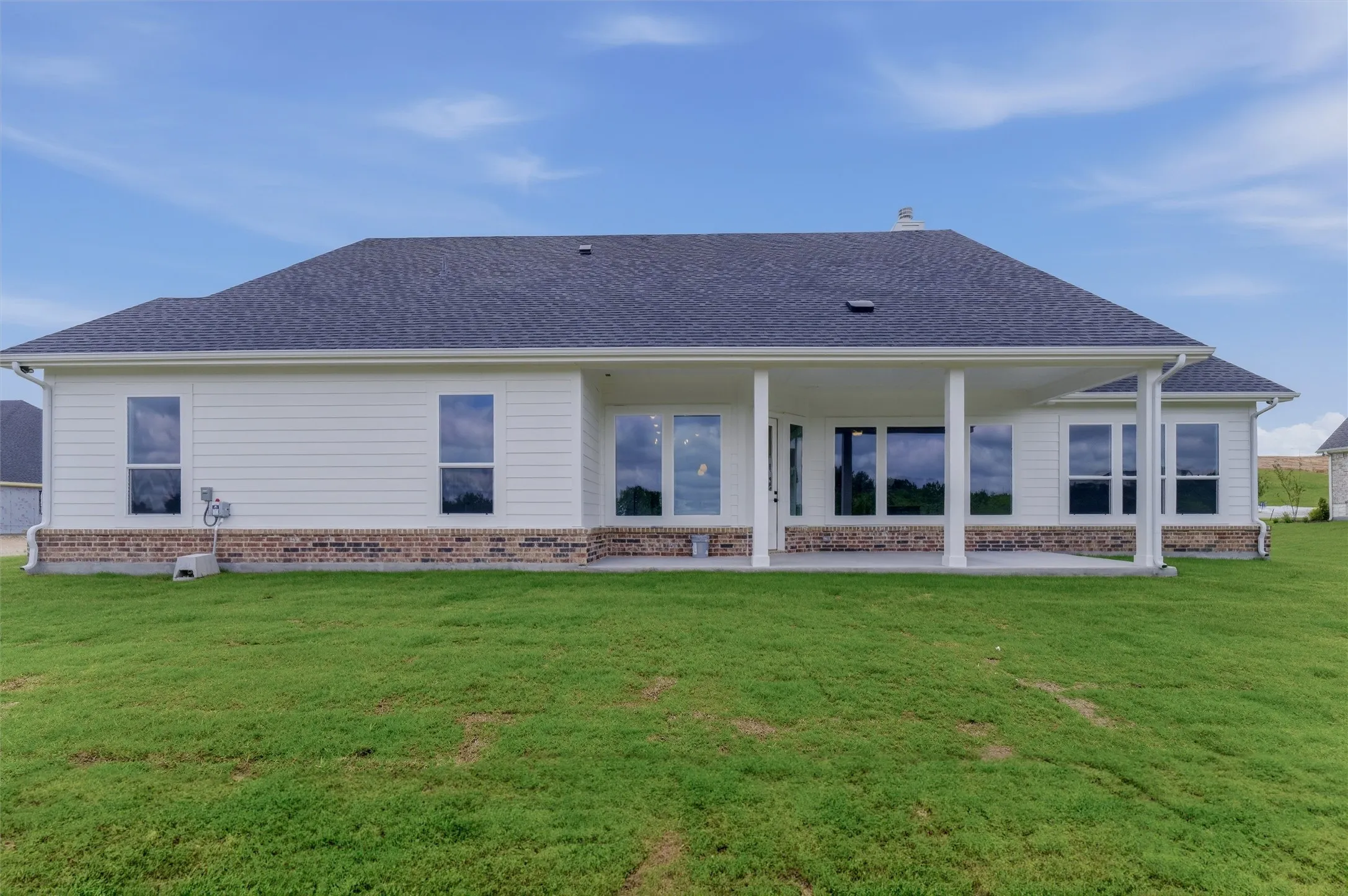 Expansive rear exterior featuring a covered patio with white columns, large windows, white siding, and a brick foundation