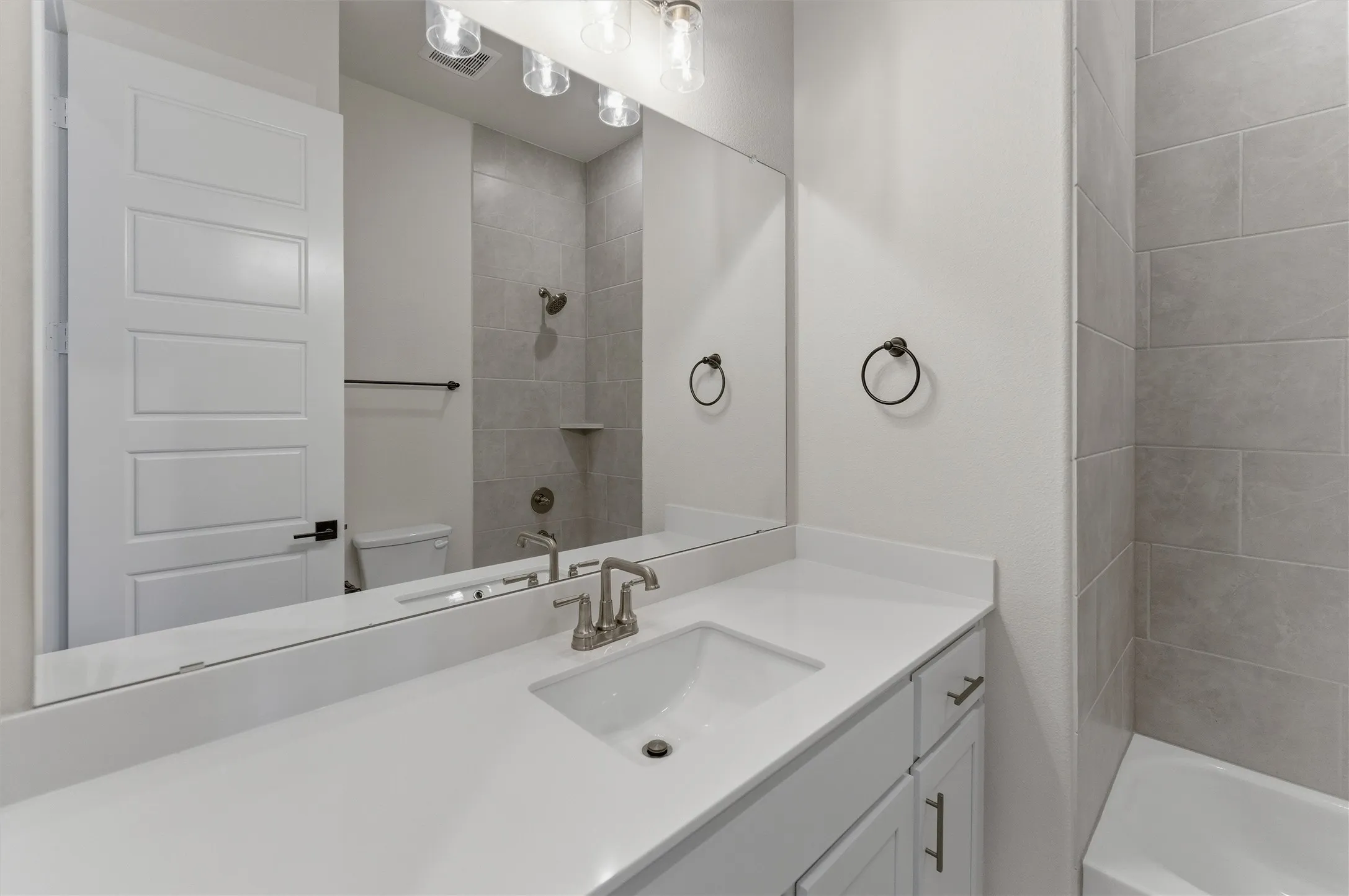 Bathroom featuring a white vanity with an integrated sink, brushed nickel faucet, large wall-mounted mirror, and overhead vanity lighting