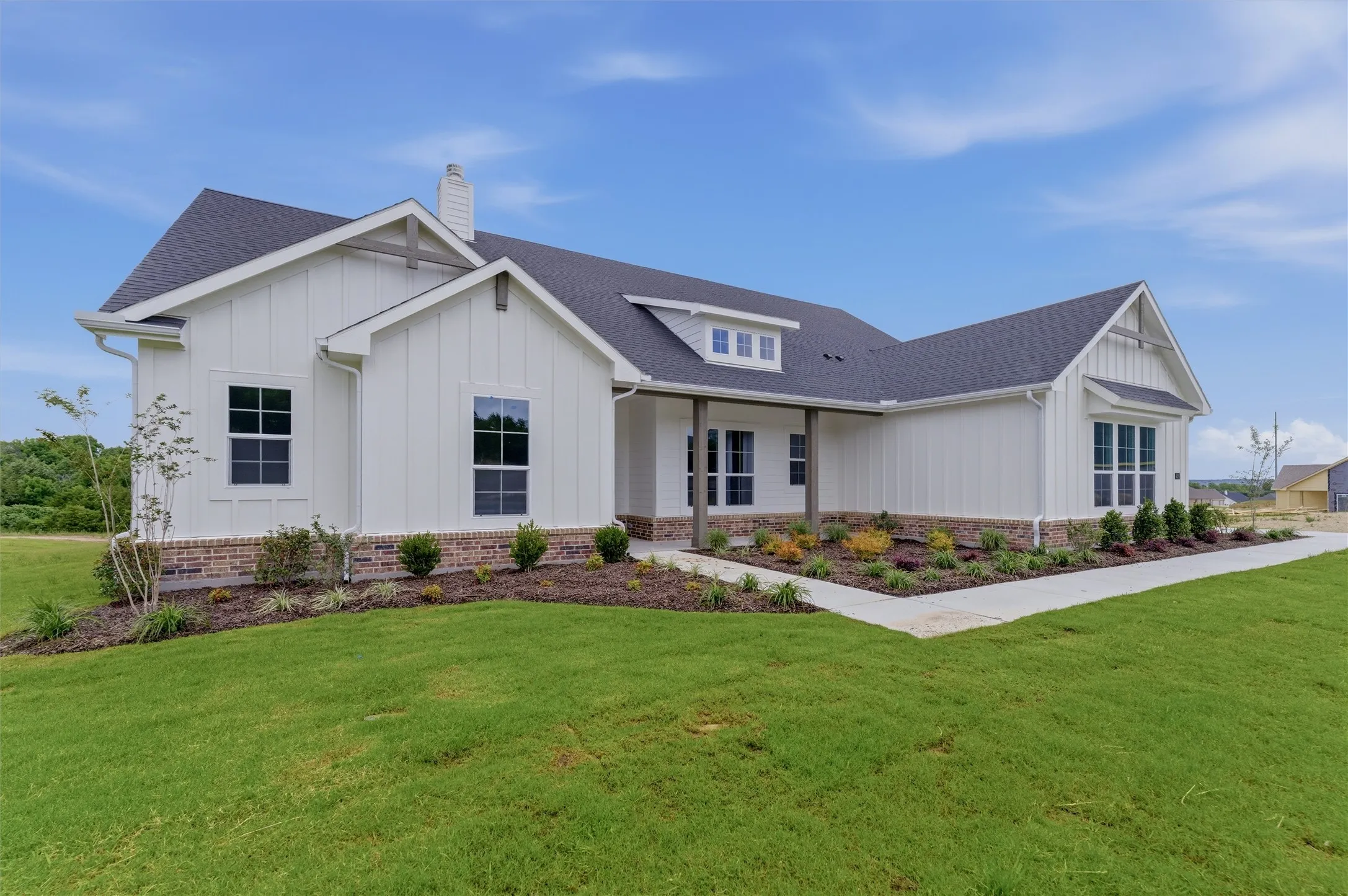 Modern farmhouse exterior with white board-and-batten siding, a dark shingle roof, and brick foundation accents