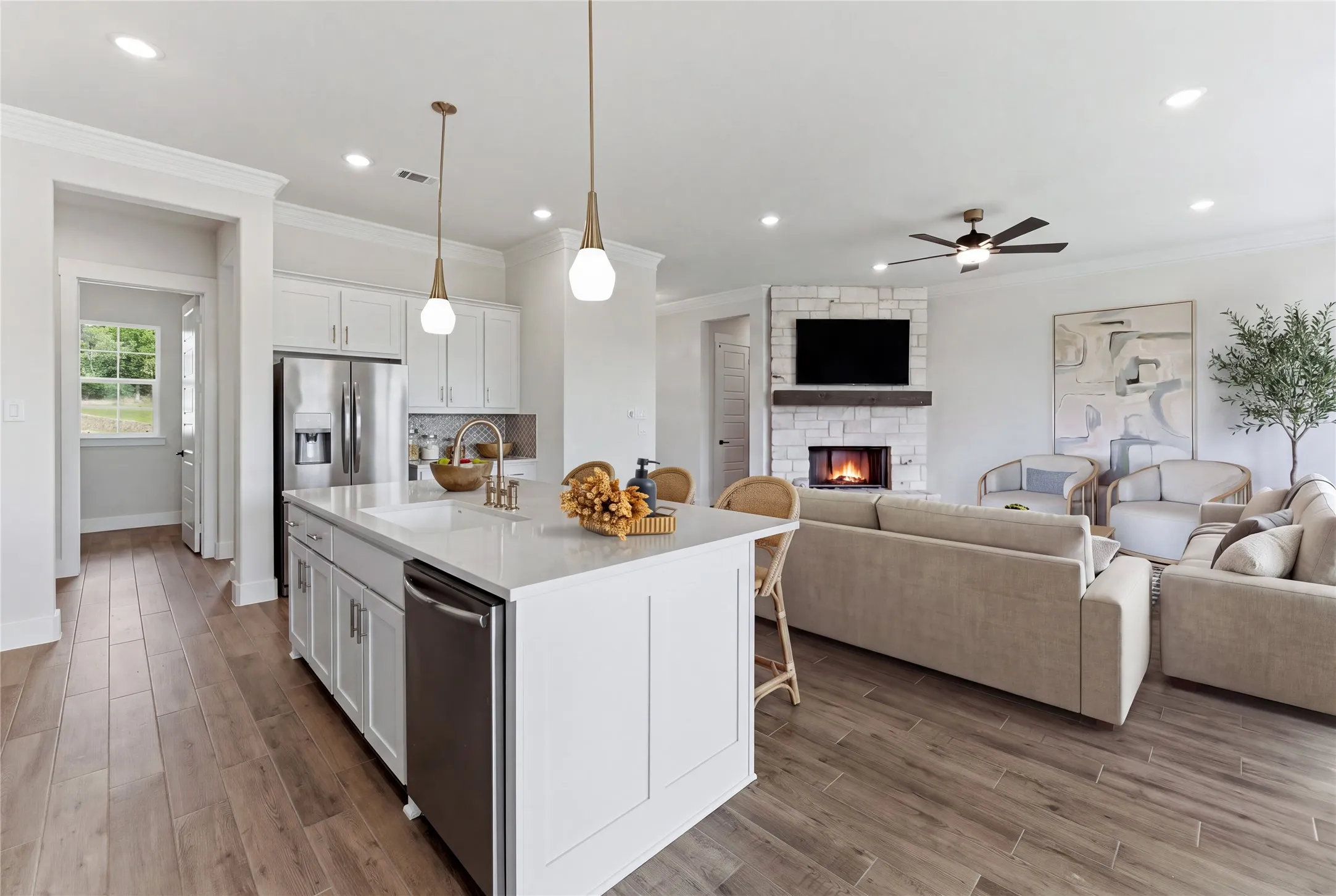 Spacious open-concept layout featuring wood-finish flooring, a kitchen island with pendant lighting, white cabinetry, and stainless steel appliances