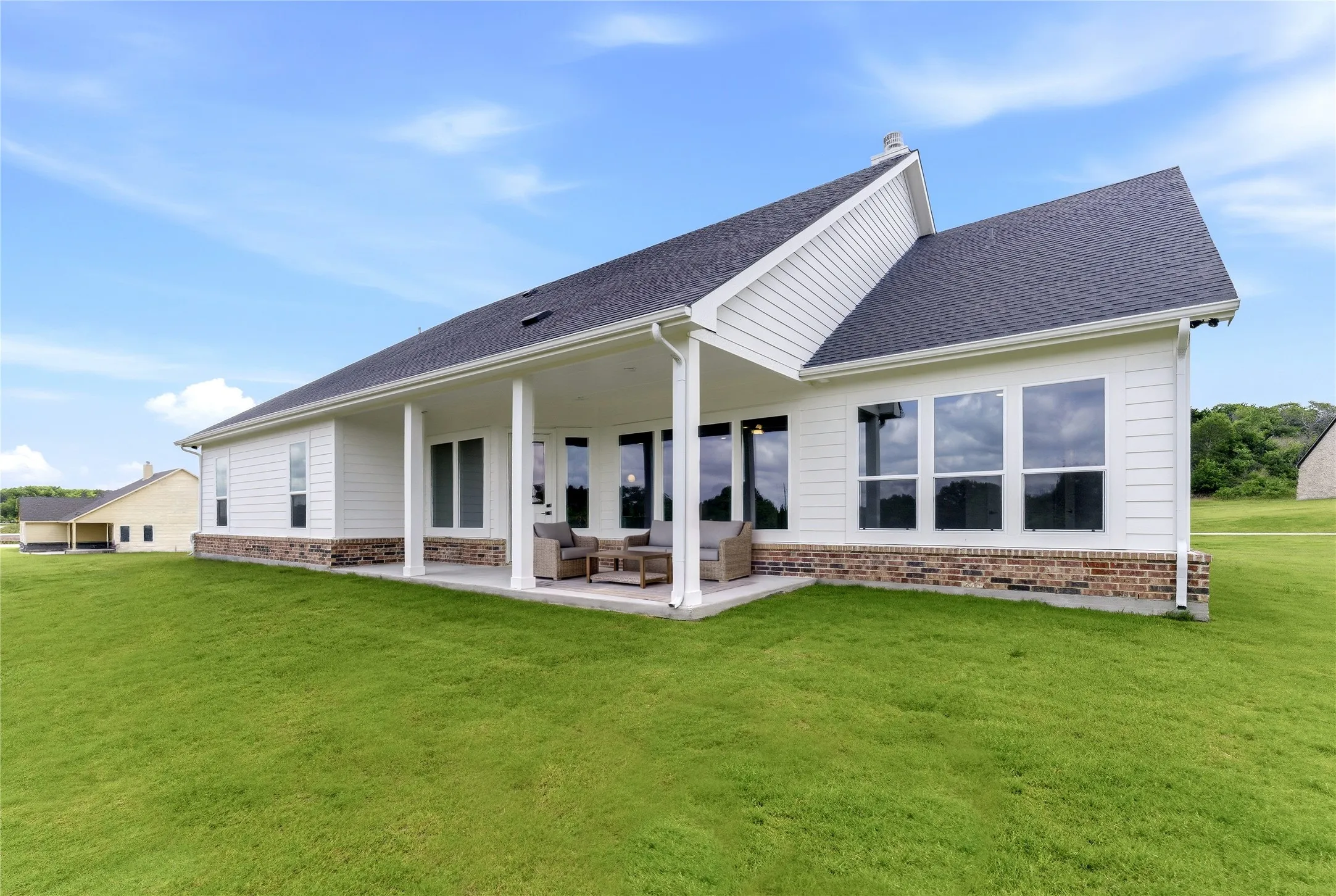 Expansive backyard featuring a covered patio, multiple large windows, white siding, and a brick foundation