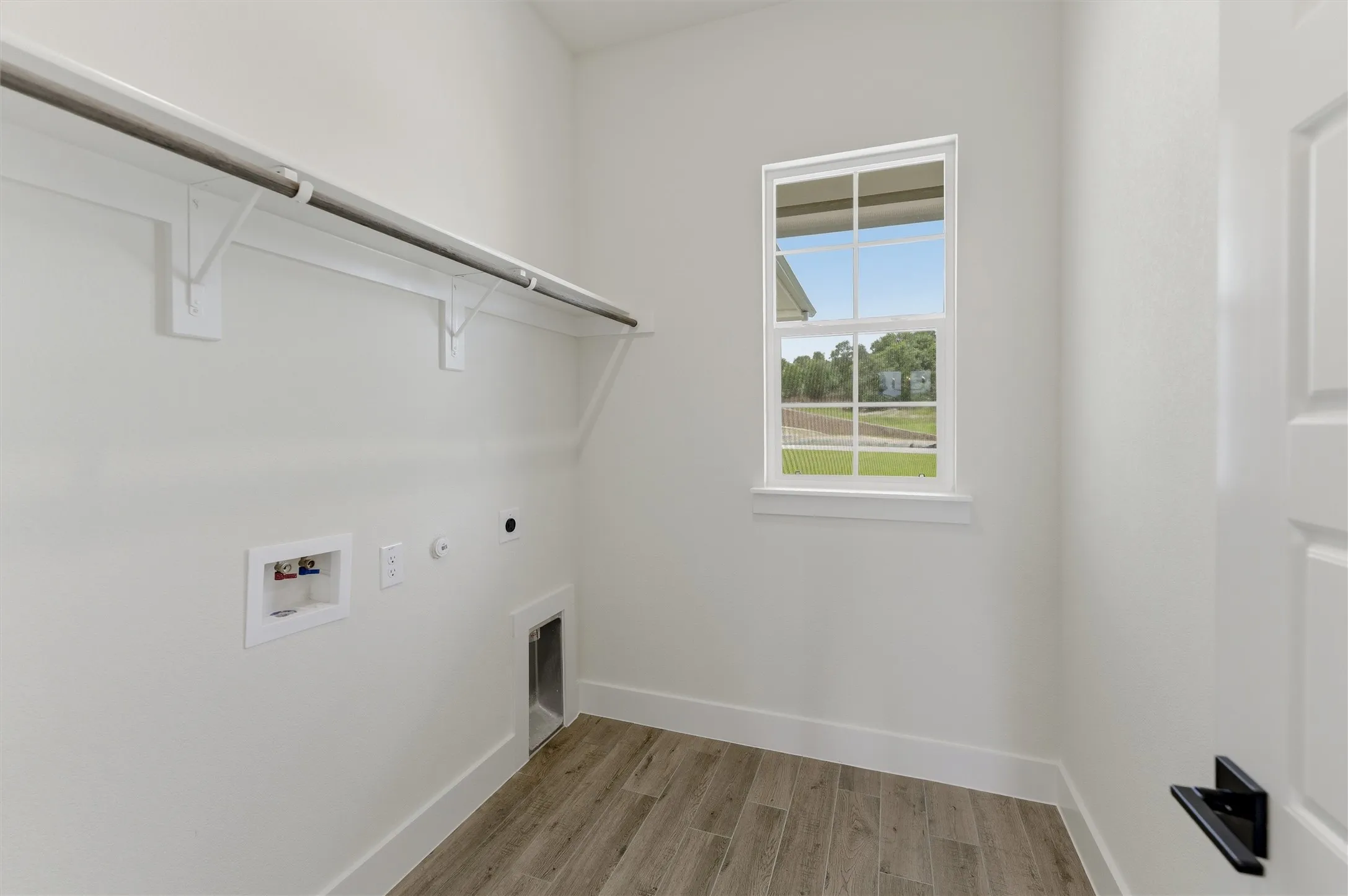 Dedicated laundry room featuring wood-finish flooring, a multipane window, and a built-in hanging rod with shelving