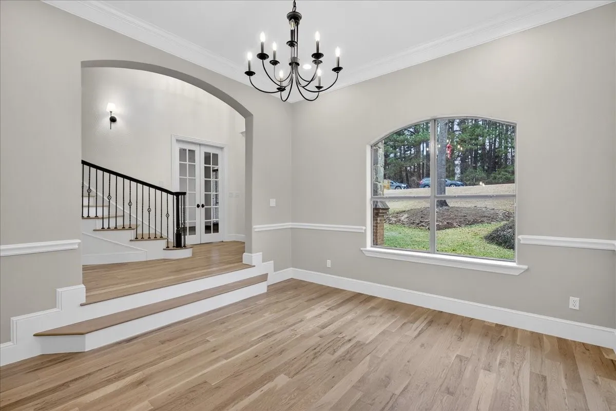 Unfurnished dining area featuring arched walkways, ornamental molding, light wood-style floors, suspended lighting, and french doors