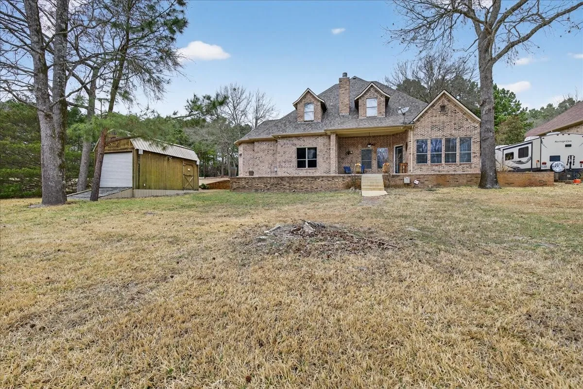 View of front of house with covered porch, a front lawn, an outbuilding, and brick siding