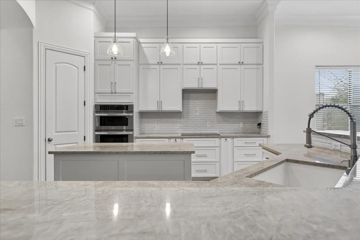 Kitchen featuring crown molding, white cabinets, light stone counters, double oven, and pendant lighting