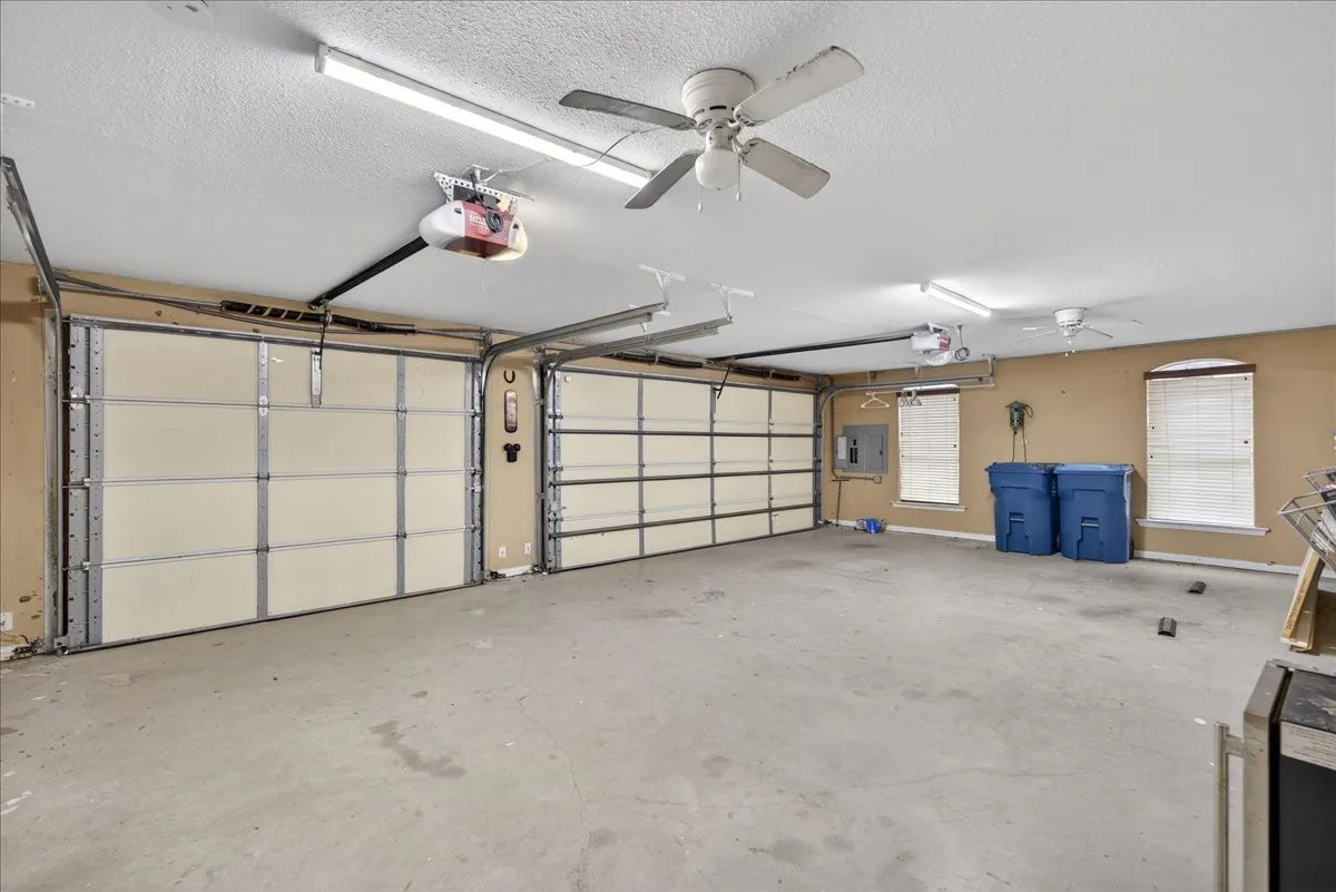 Garage with ceiling fan, a garage door opener, and electric panel