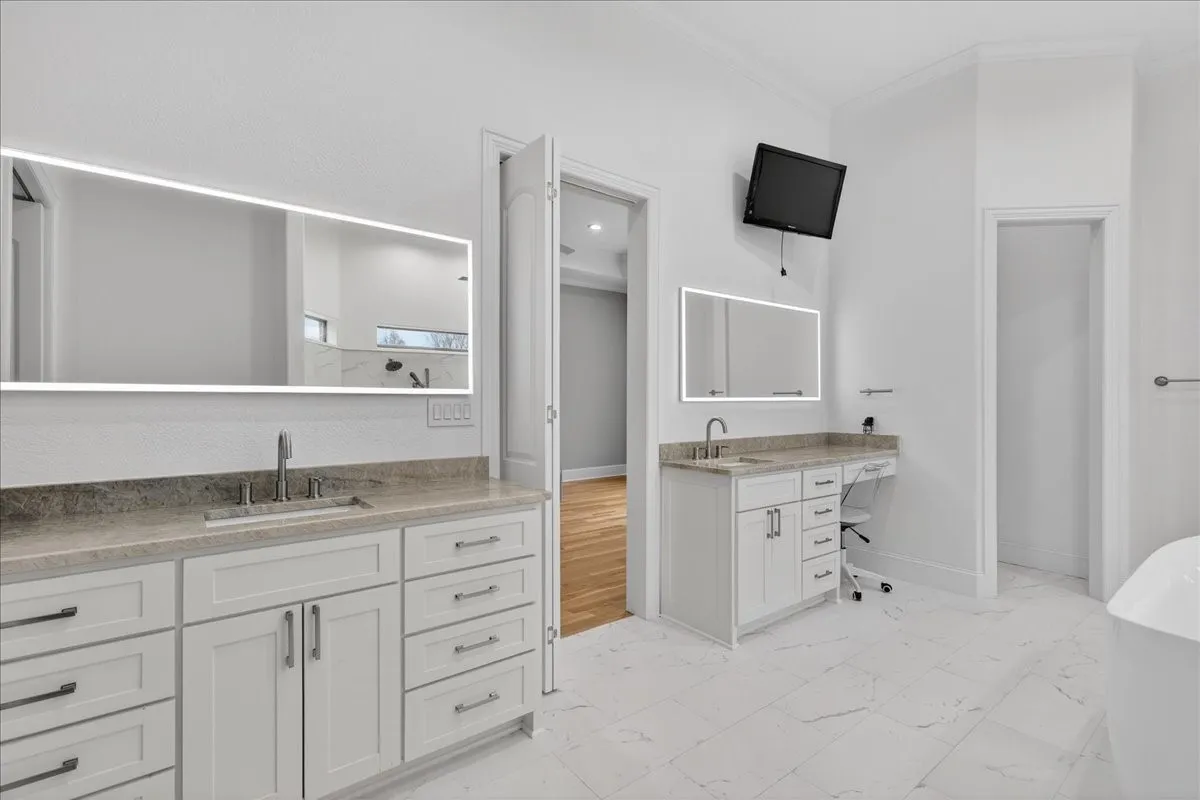 Full bathroom with light marble finish floors, ornamental molding, two vanities, and a soaking tub