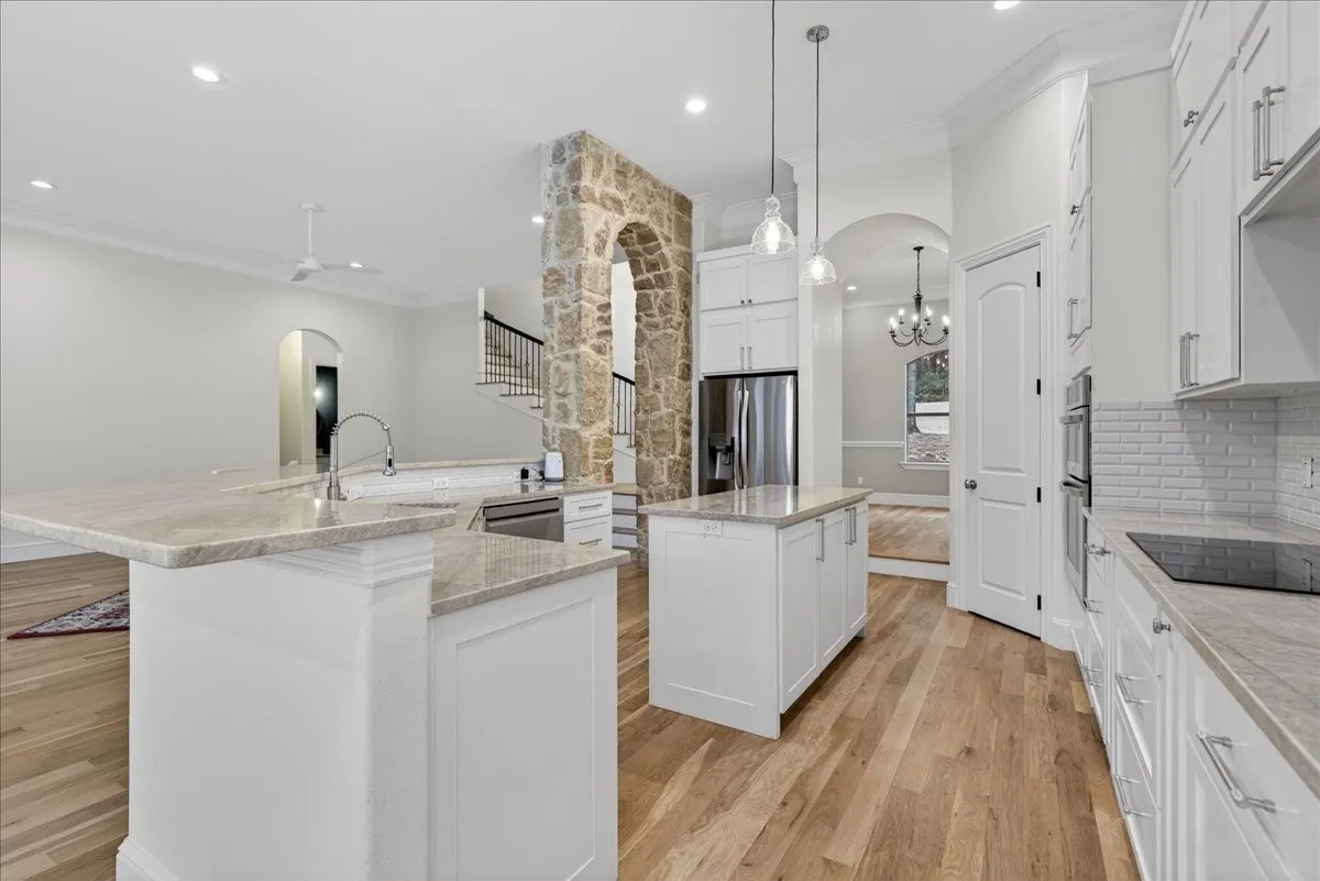 Kitchen featuring arched walkways, crown molding, light wood-style floors, white cabinetry, and light stone countertops