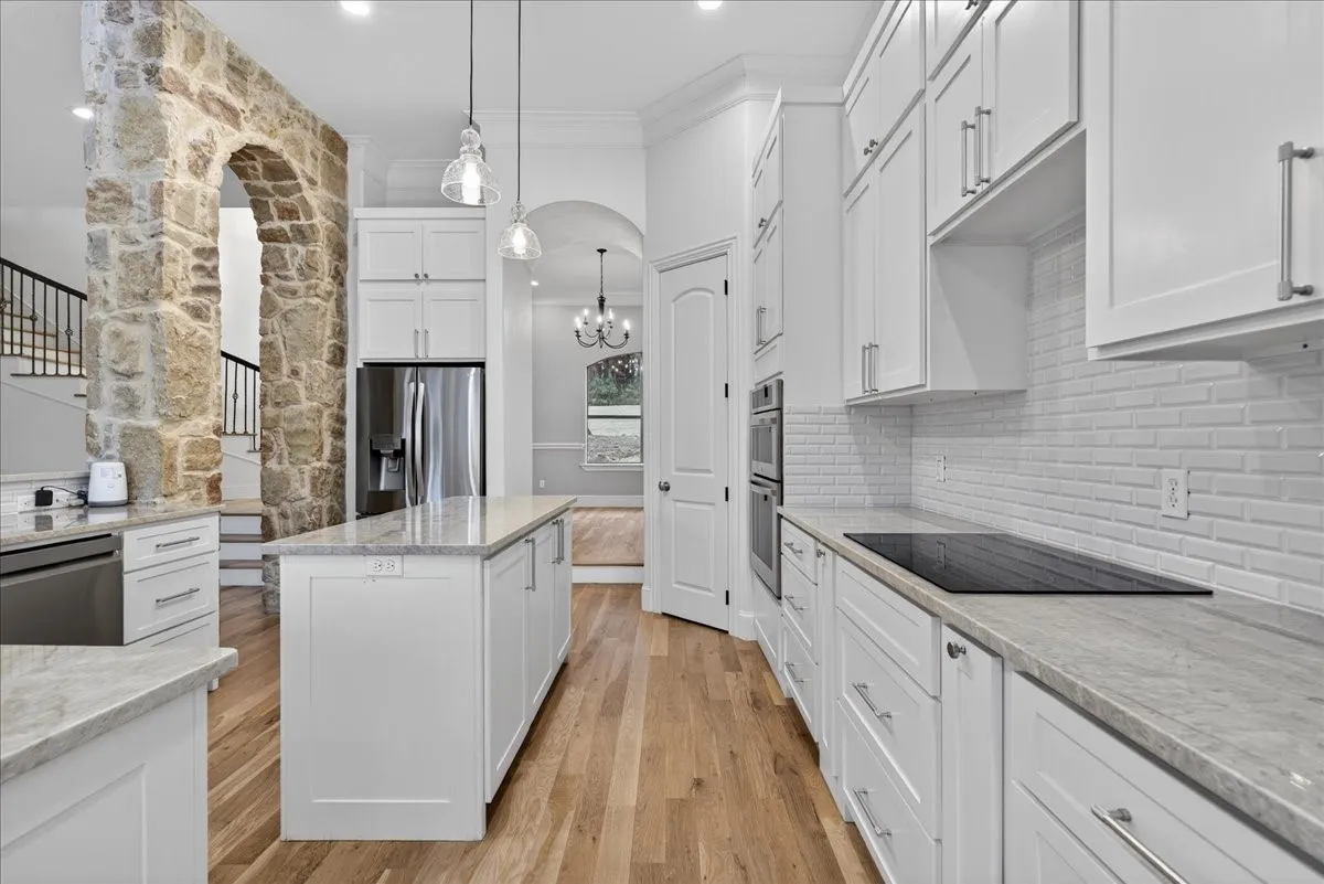 Kitchen with arched walkways, white cabinetry, ornamental molding, light wood-type flooring, and stainless steel appliances