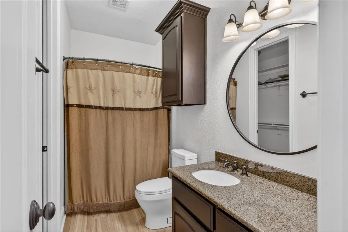 Bathroom with vanity, a shower with shower curtain, light wood-style flooring, a walk in closet, and a textured wall