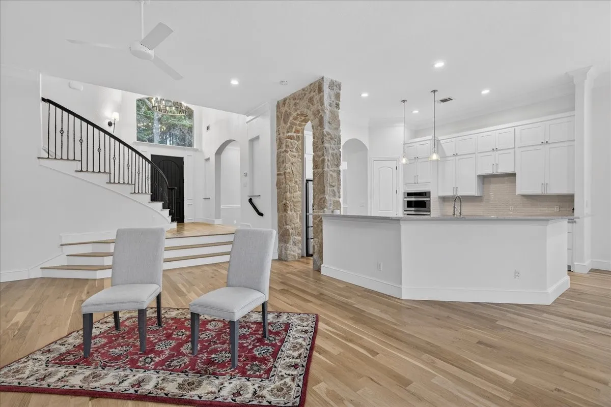Kitchen with arched walkways, white cabinets, light wood finished floors, hanging light fixtures, and a ceiling fan