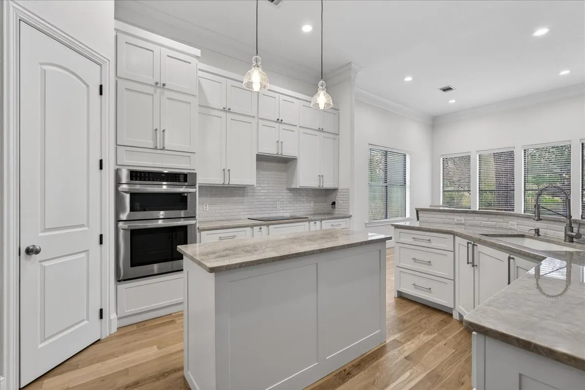 Kitchen with crown molding, stainless steel double oven, backsplash, light stone counters, and light wood-type flooring