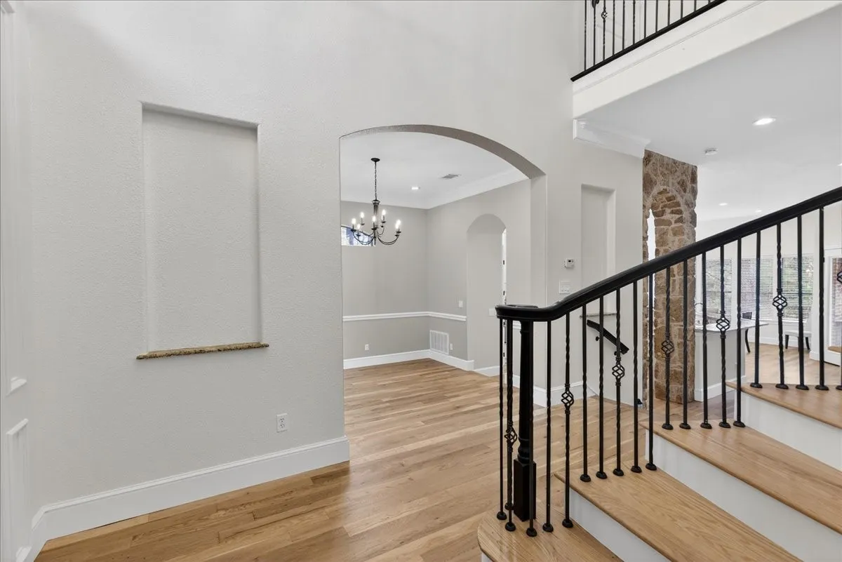 Stairs featuring wood finished floors, arched walkways, crown molding, suspended lighting, and a high ceiling