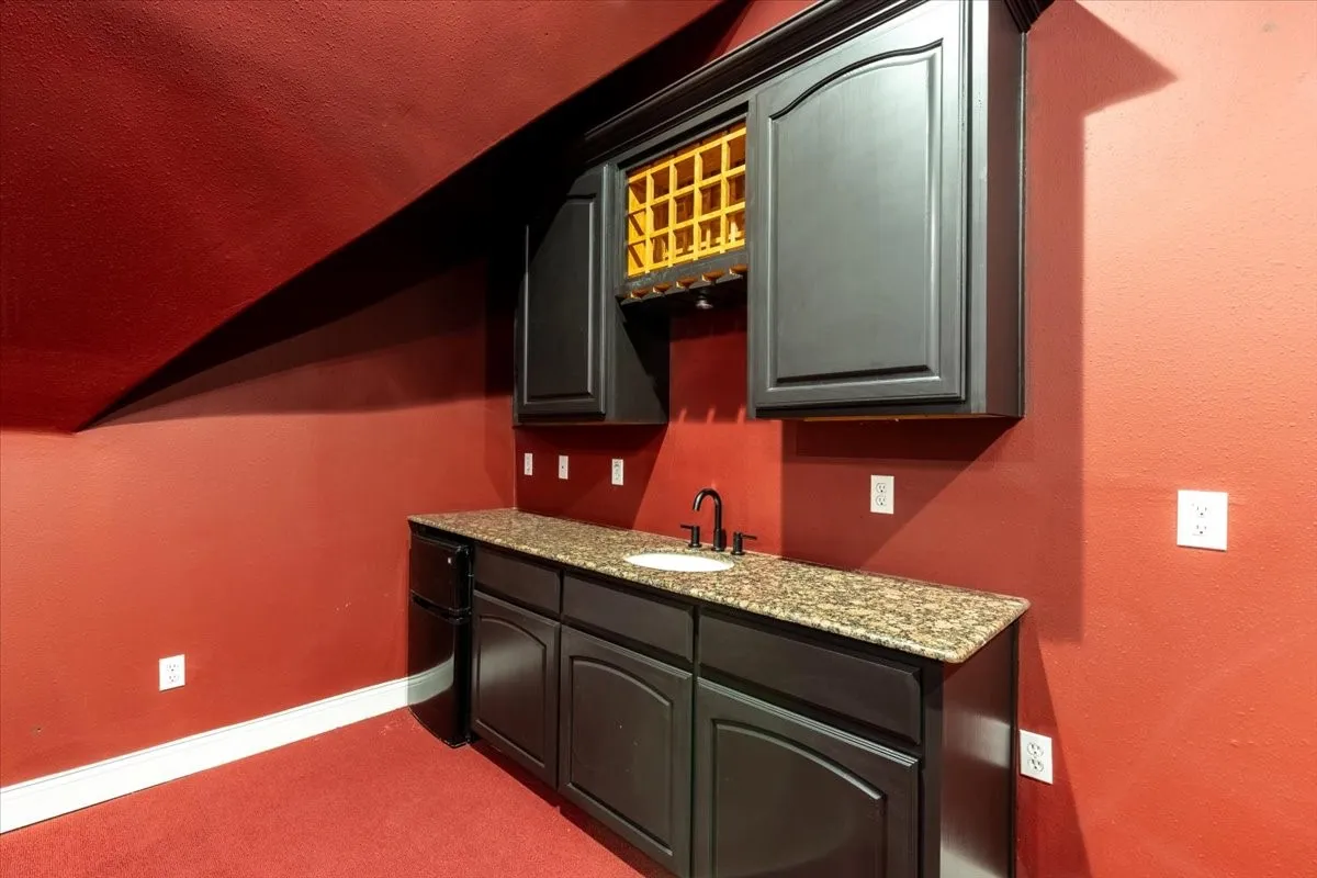 Indoor wet bar with light stone counters, dark carpet, and lofted ceiling