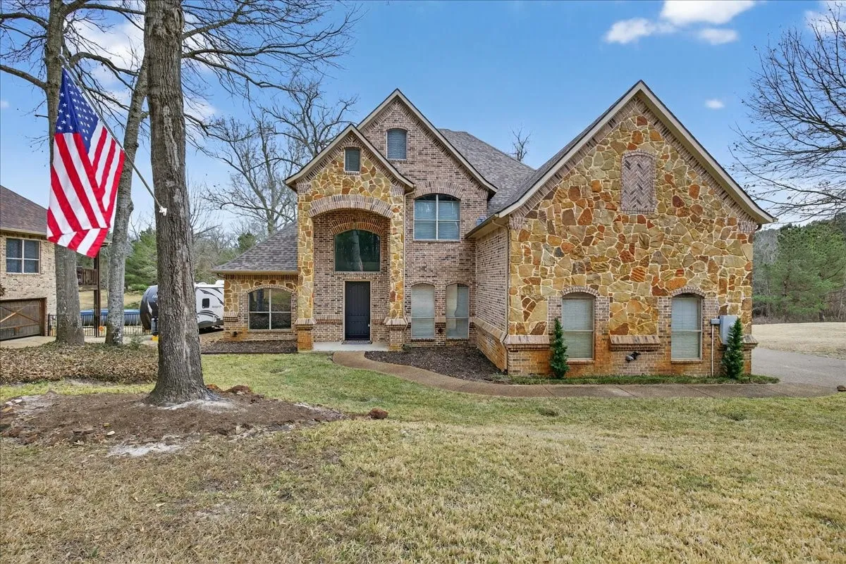 French country home with brick siding, stone siding, and a front lawn