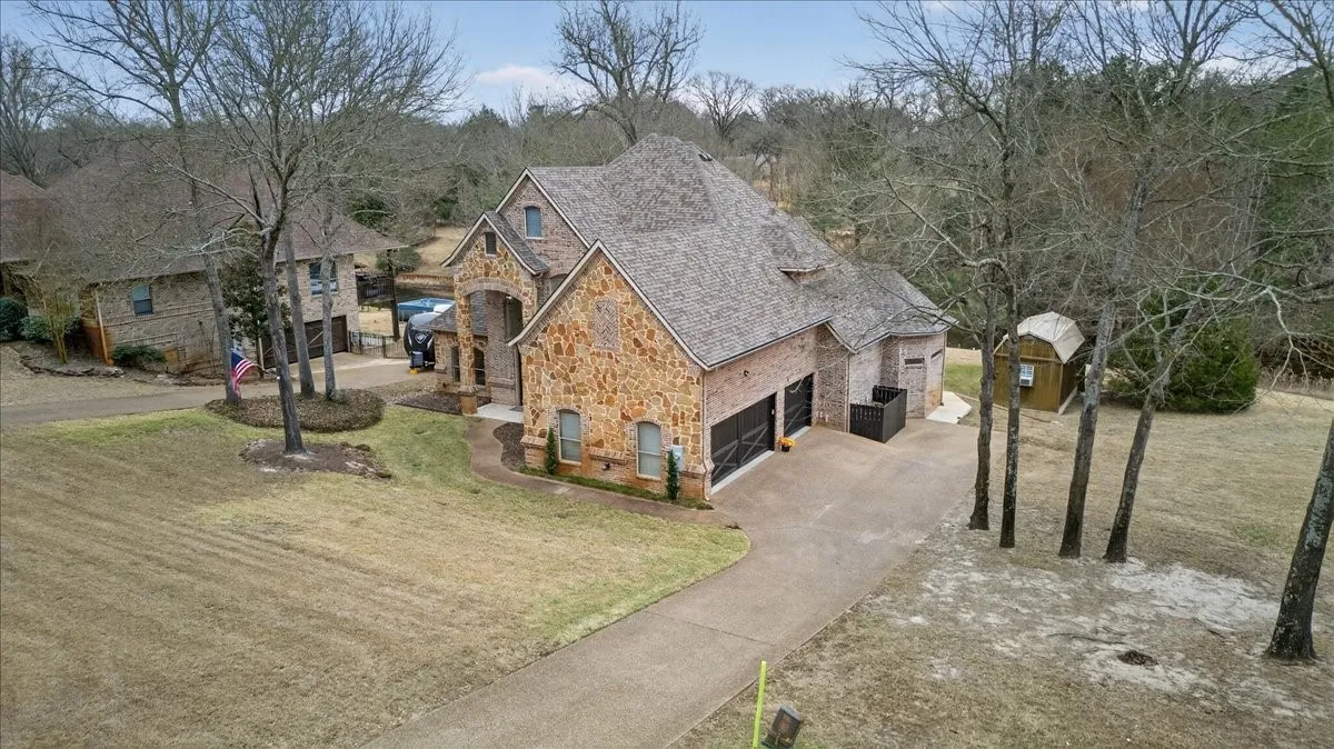View of front of property with stone siding, a front lawn, driveway, a storage unit, and a garage
