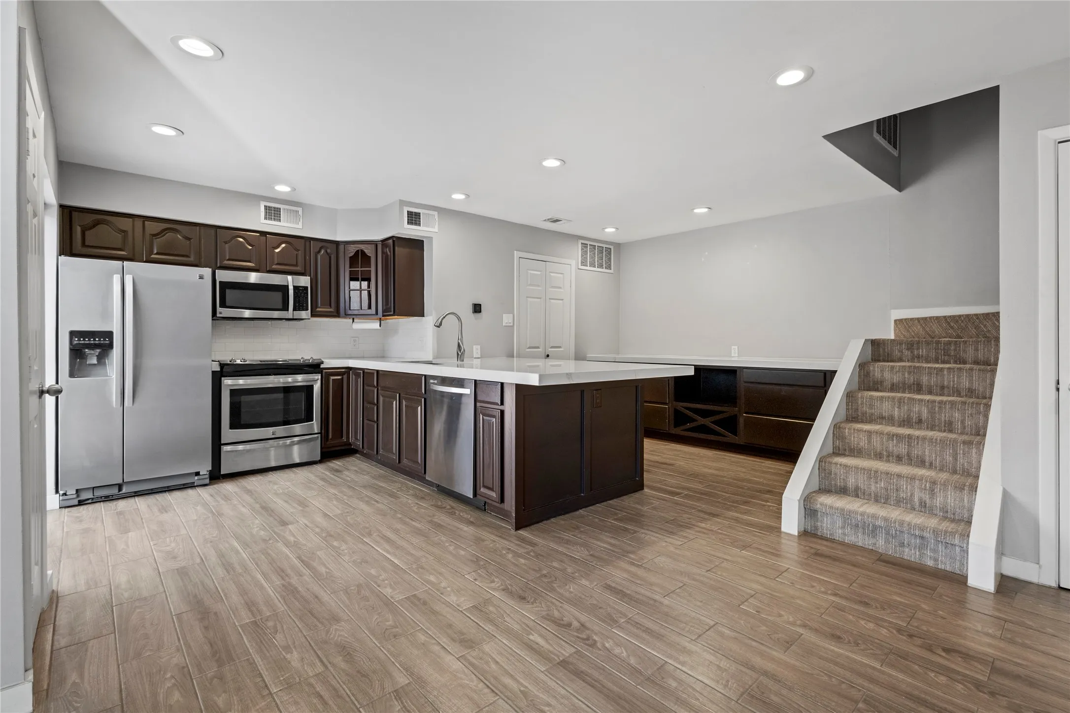 Kitchen with kitchen peninsula, light hardwood / wood-style flooring, dark brown cabinets, appliances with stainless steel finishes, and backsplash