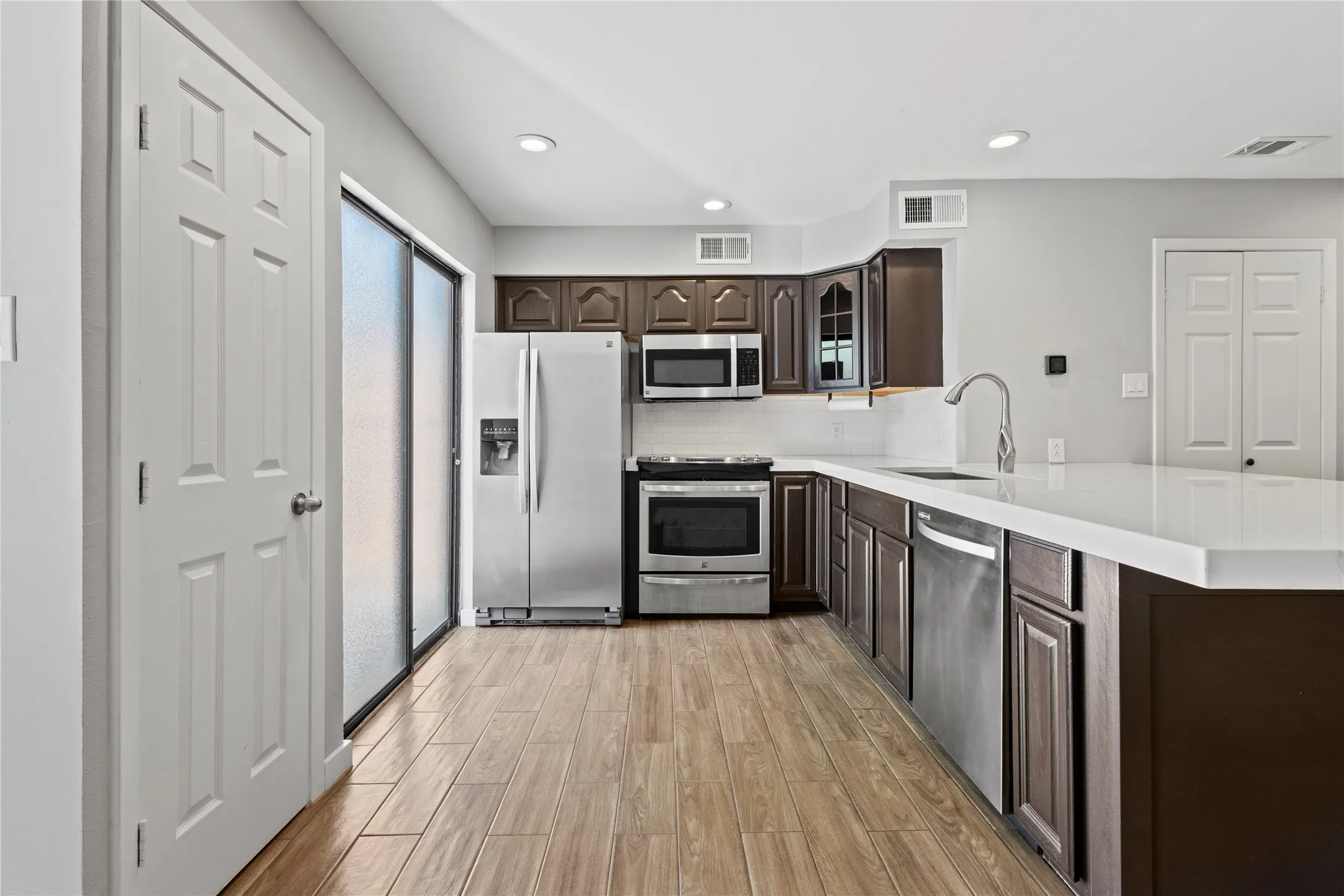 Kitchen featuring light hardwood / wood-style floors, stainless steel appliances, dark brown cabinets, backsplash, and sink