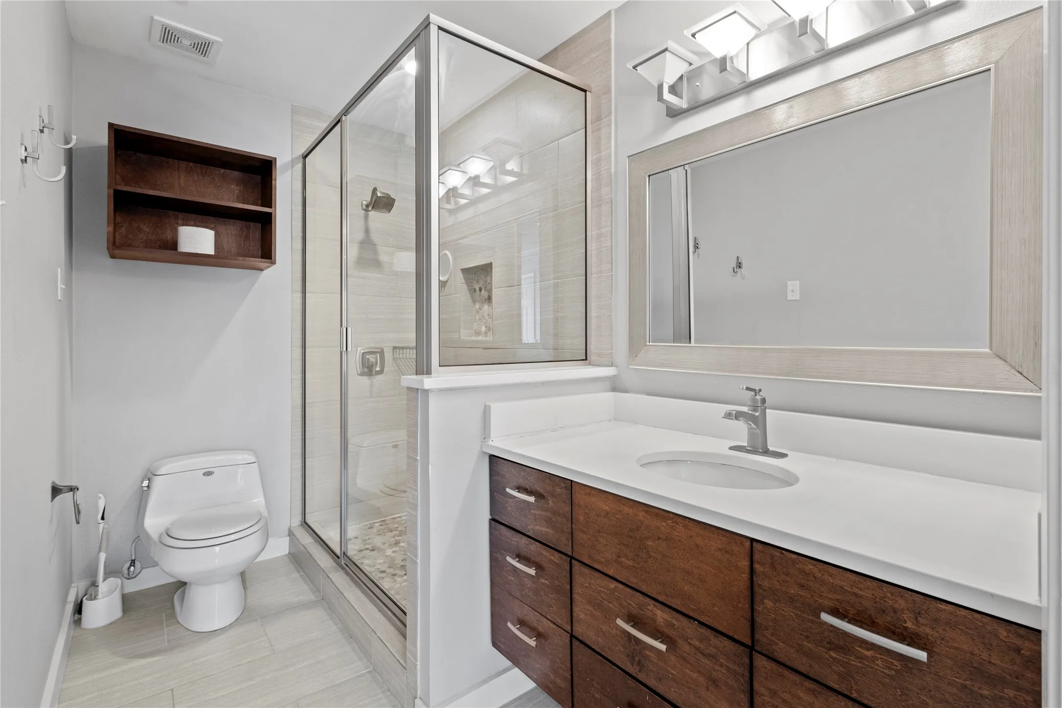 Bathroom with an enclosed shower, toilet, vanity, and tile flooring