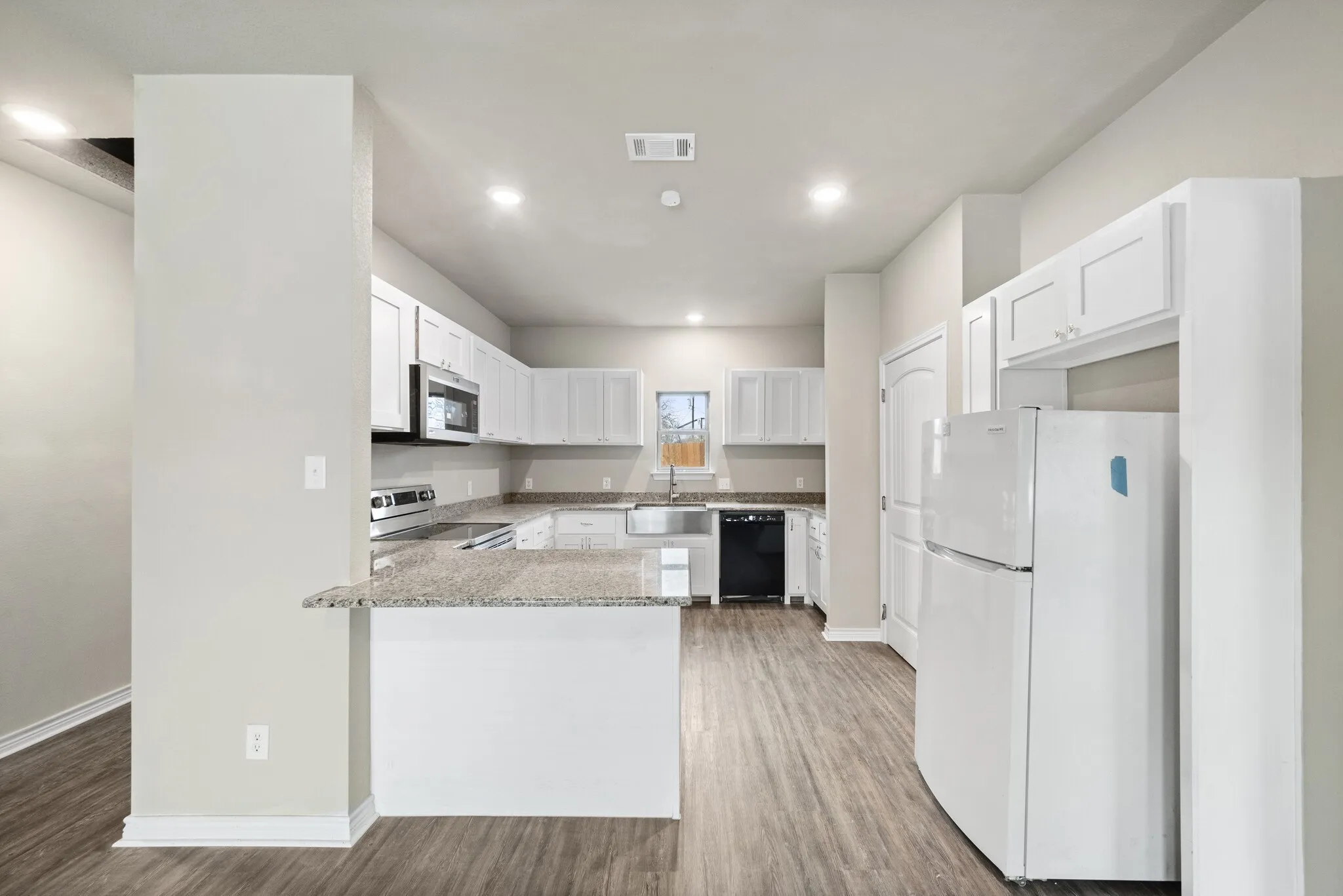 Kitchen with stainless steel appliances, light stone countertops, light wood finished floors, white cabinets, and a peninsula
