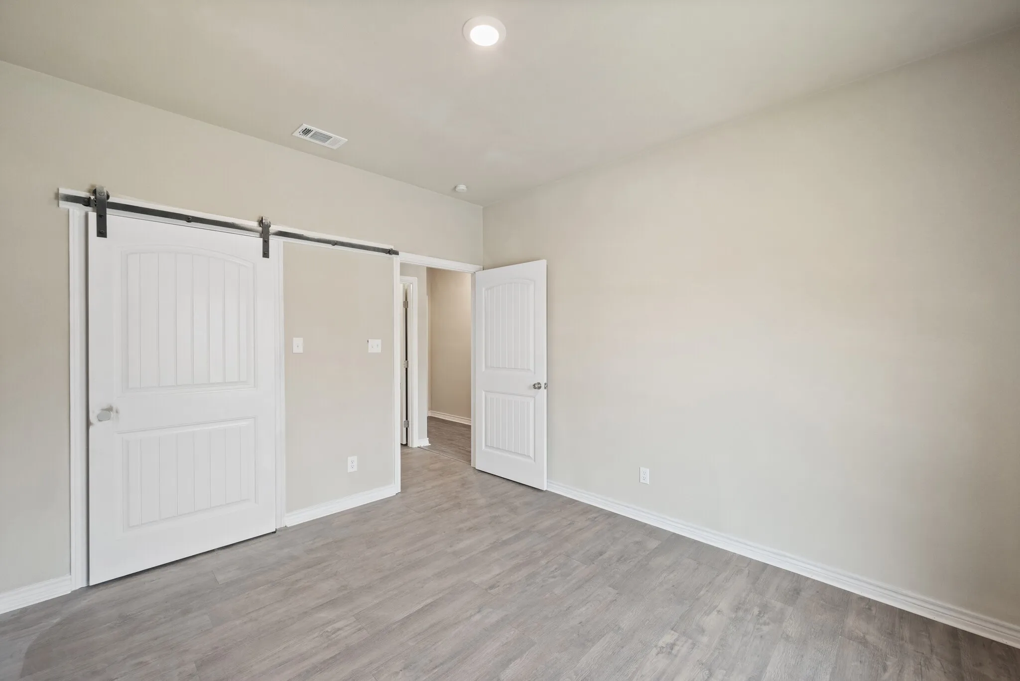 Unfurnished bedroom with a barn door, light wood finished floors, and recessed lighting