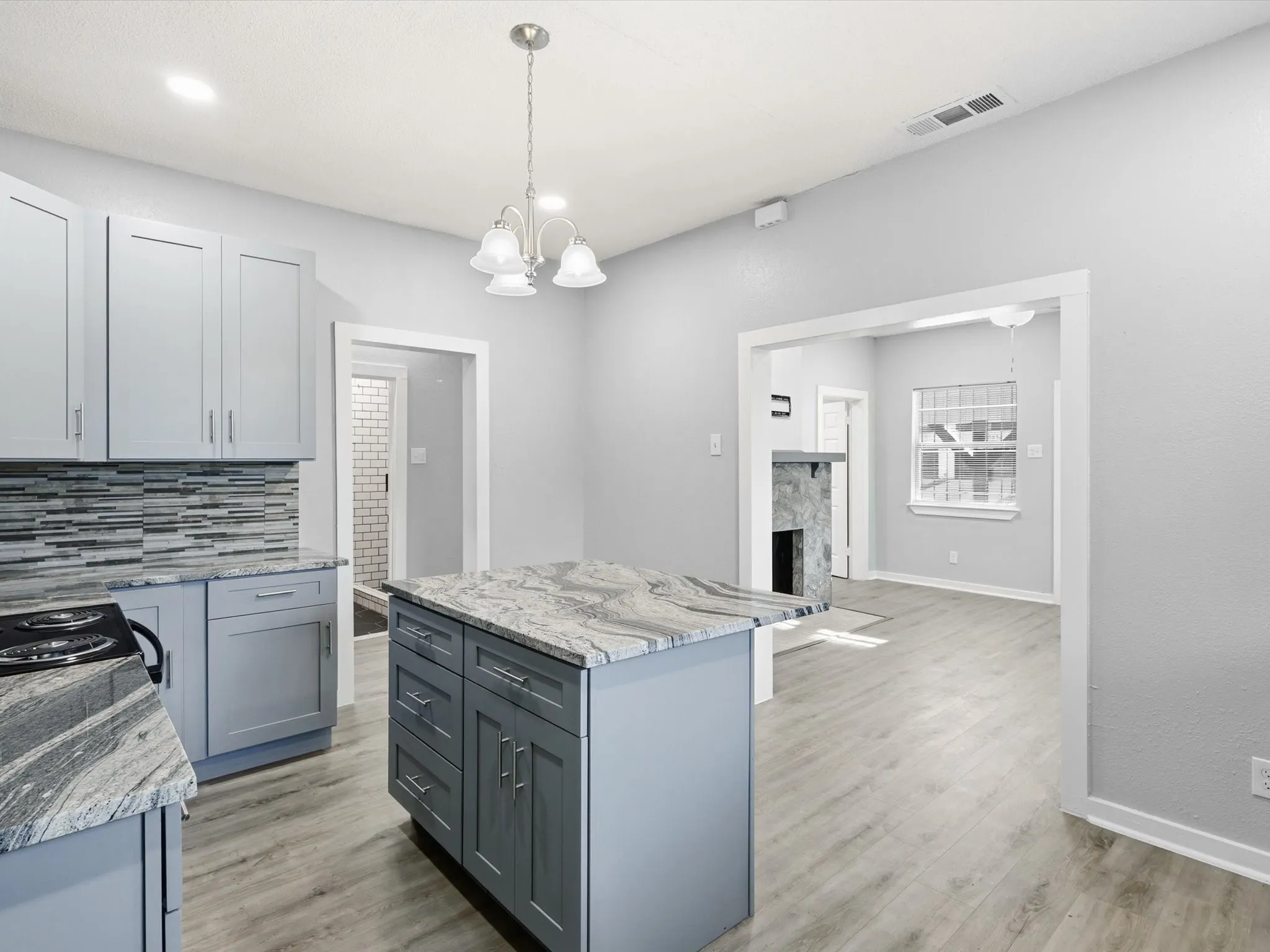 Kitchen featuring gray cabinetry, light stone countertops, a chandelier, and a kitchen island