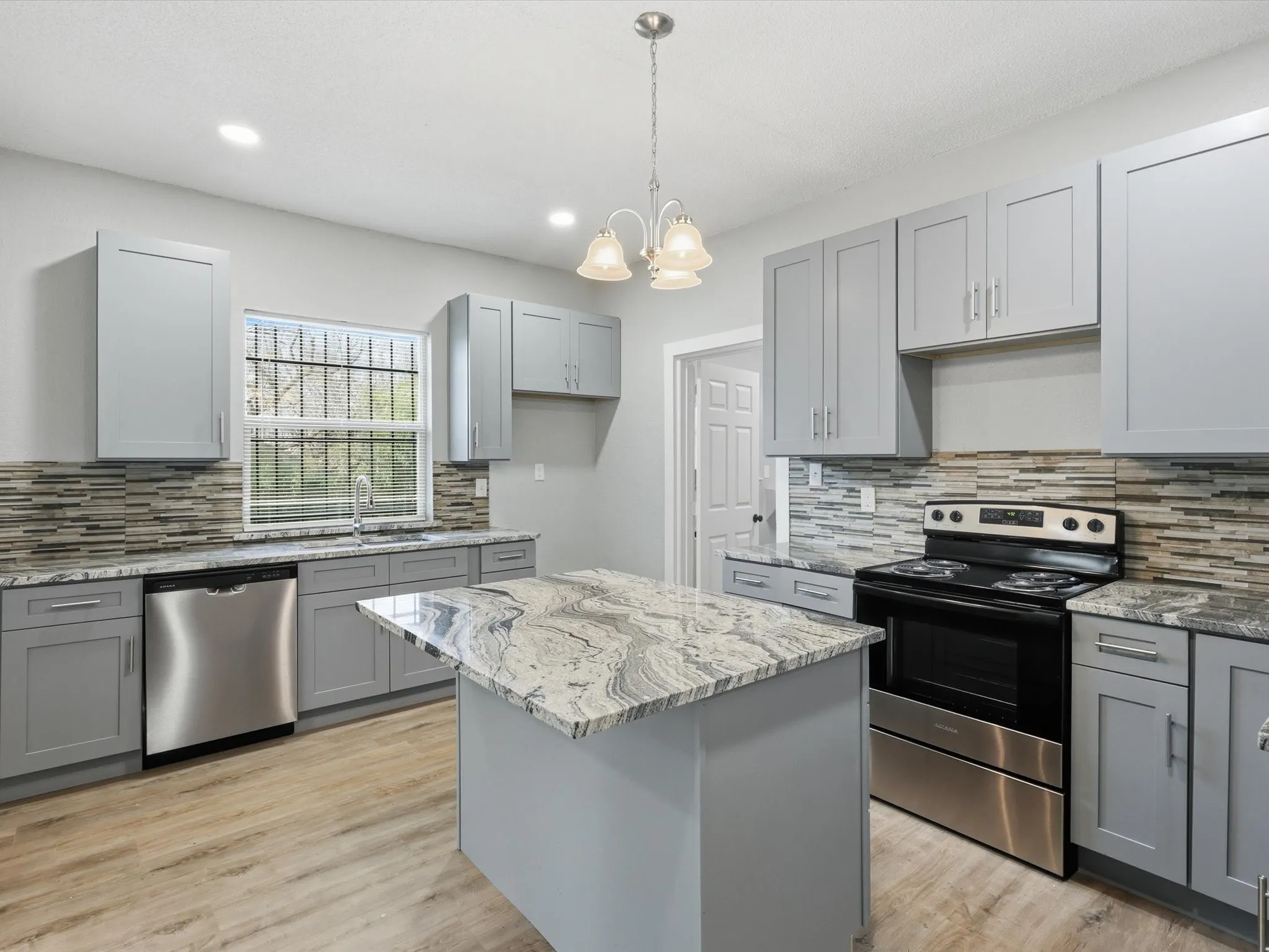 Kitchen featuring gray cabinetry, stainless steel appliances, a kitchen island, light wood-type flooring, and backsplash