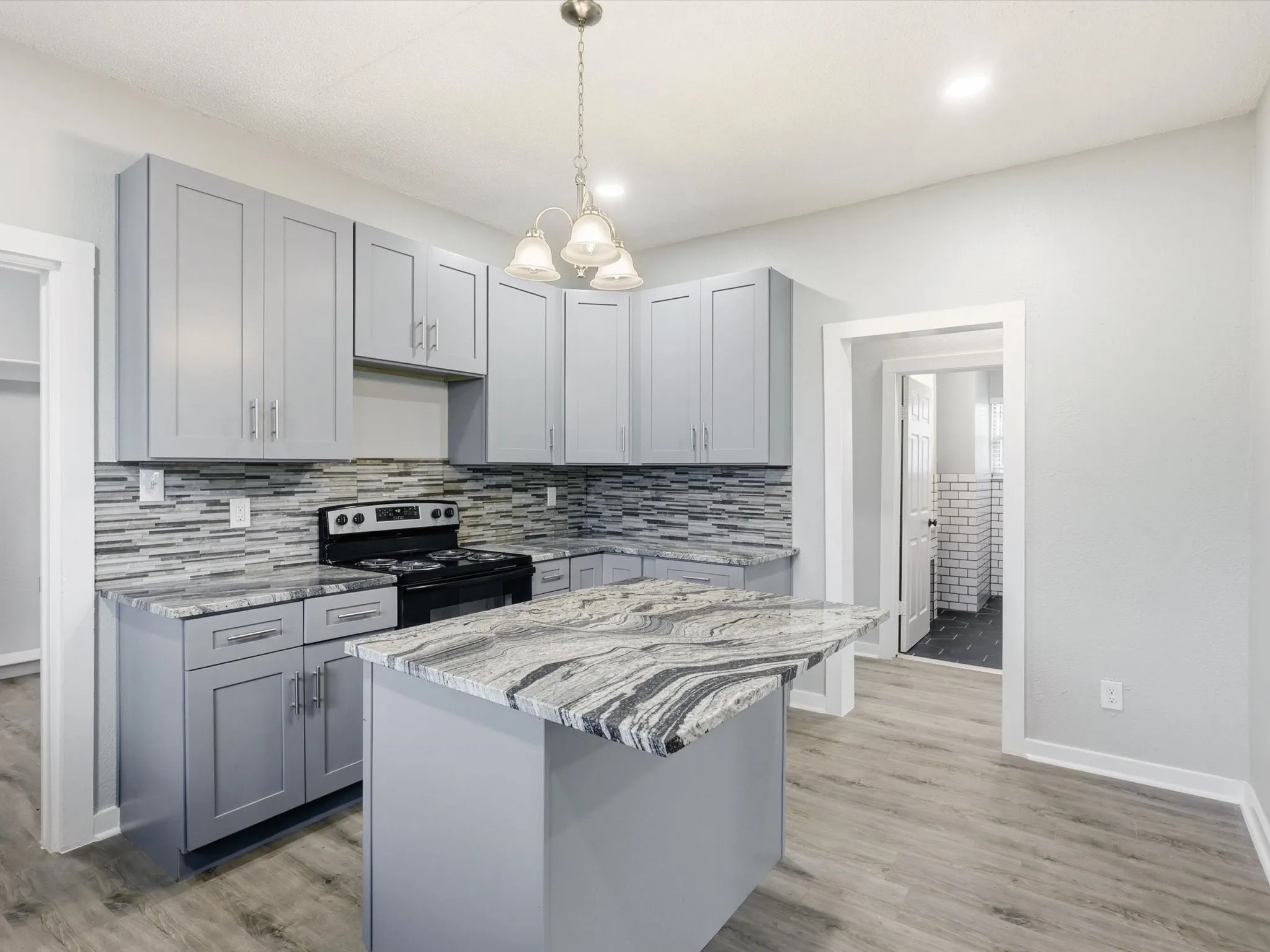 Kitchen featuring gray cabinetry, light stone countertops, stainless steel electric range, and light wood finished floors