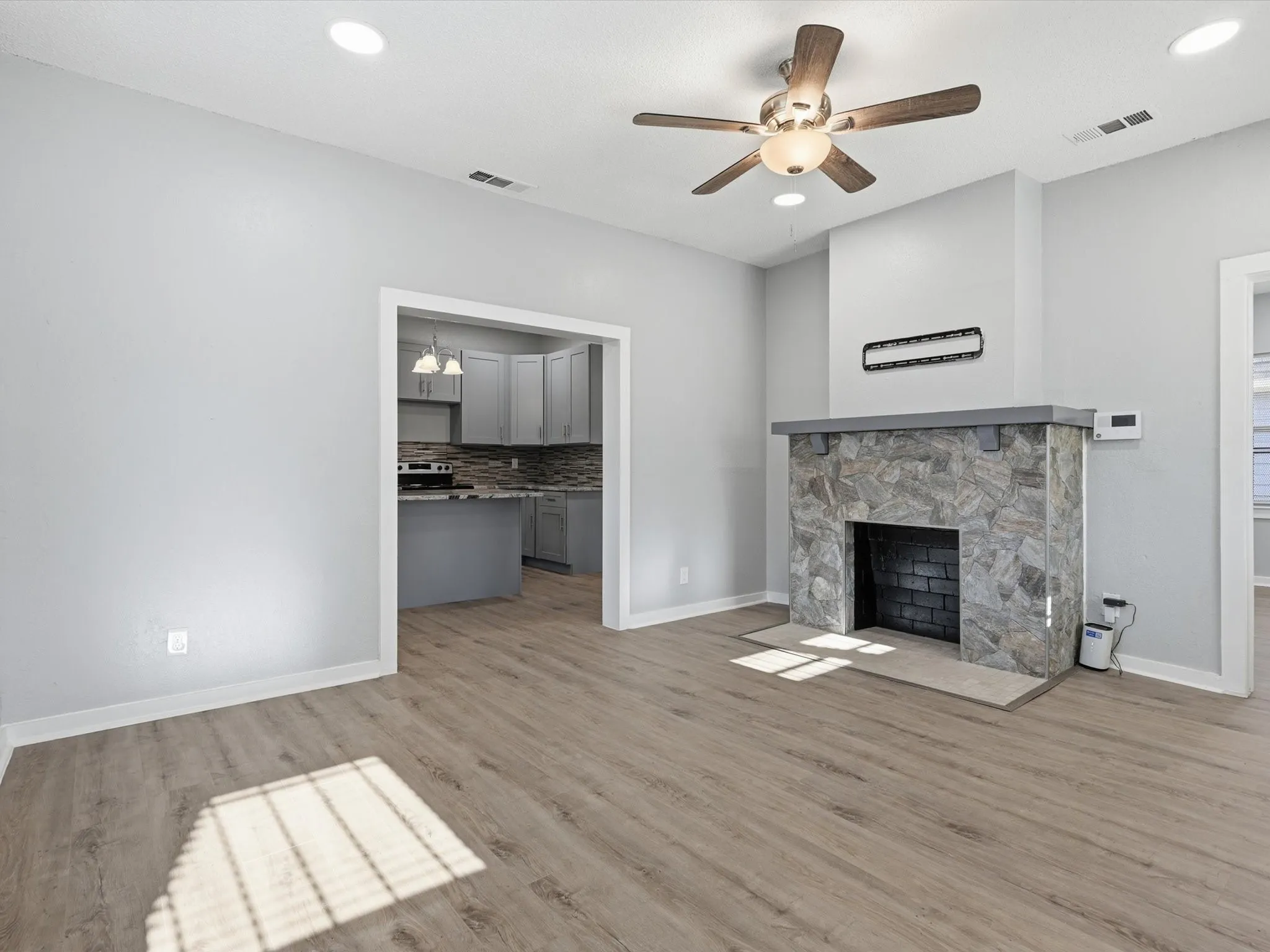 Unfurnished living room with a ceiling fan, wood finished floors, a stone fireplace, and recessed lighting