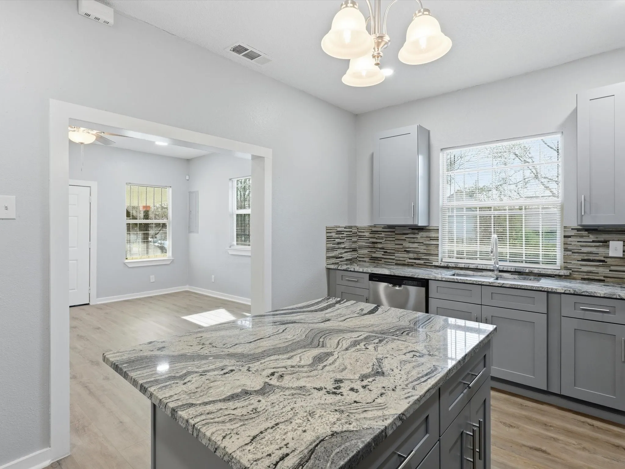 Kitchen with gray cabinetry, light stone countertops, decorative backsplash, and hanging lights