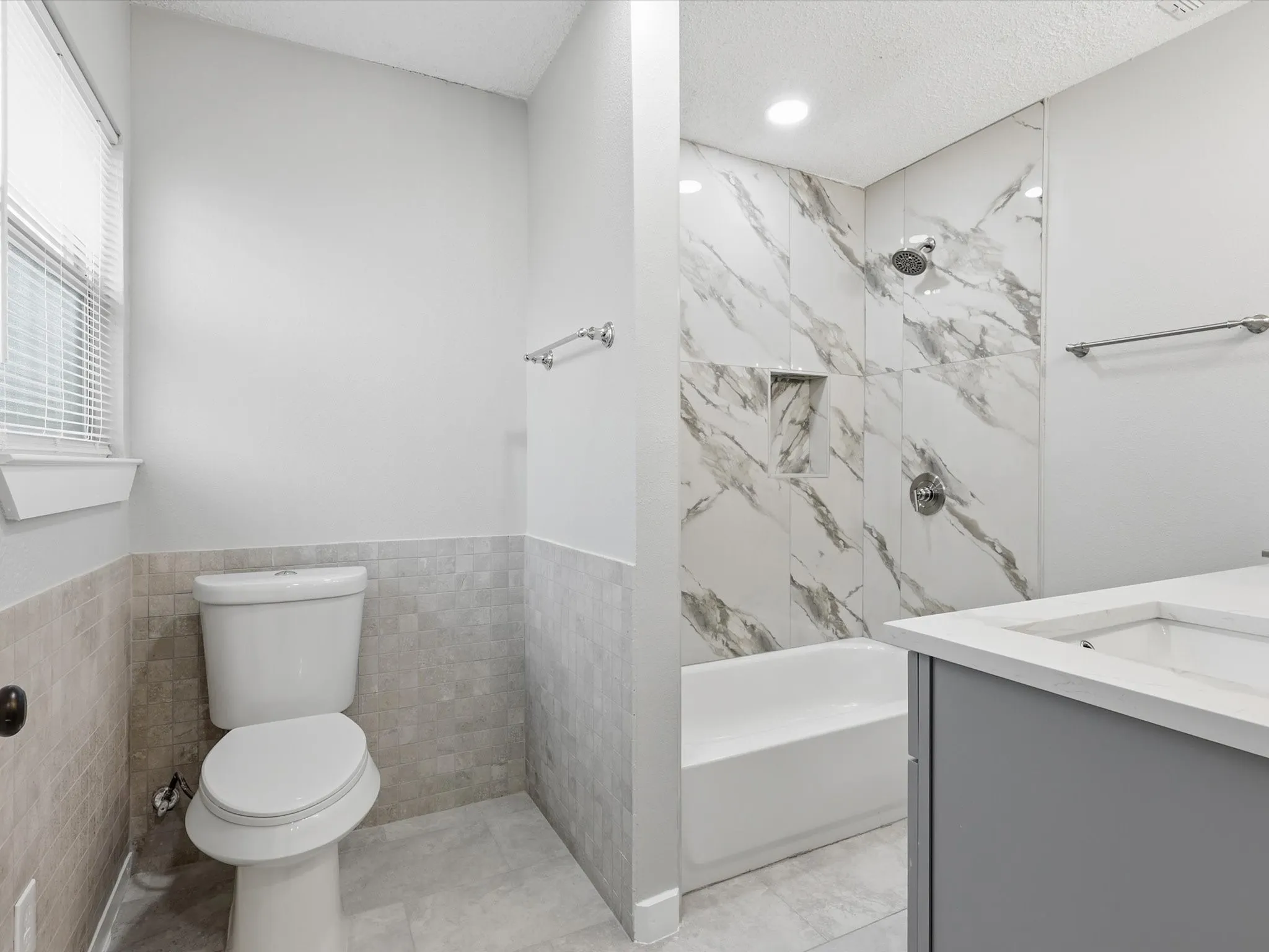Bathroom with vanity, tile walls, wainscoting, shower / tub combination, and a textured ceiling