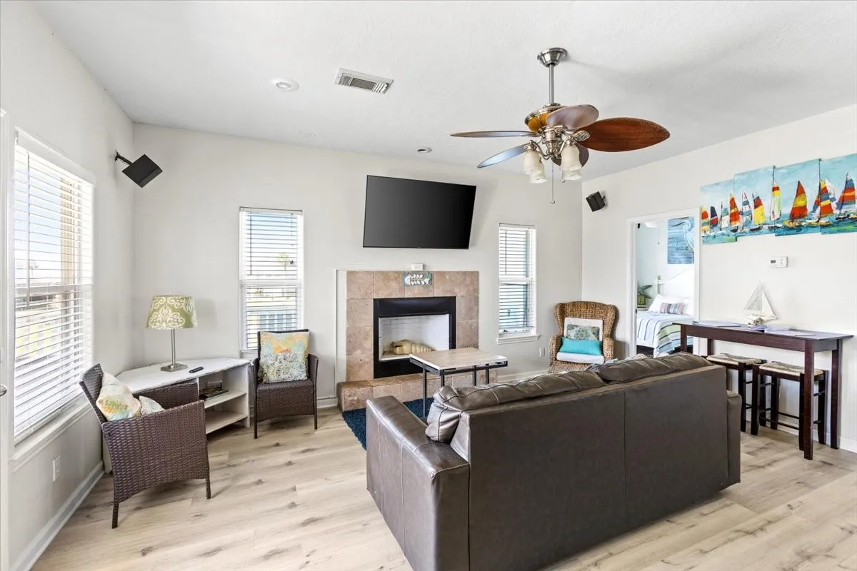 Living room with ceiling fan, light hardwood / wood-style floors, a tile fireplace, and a healthy amount of sunlight