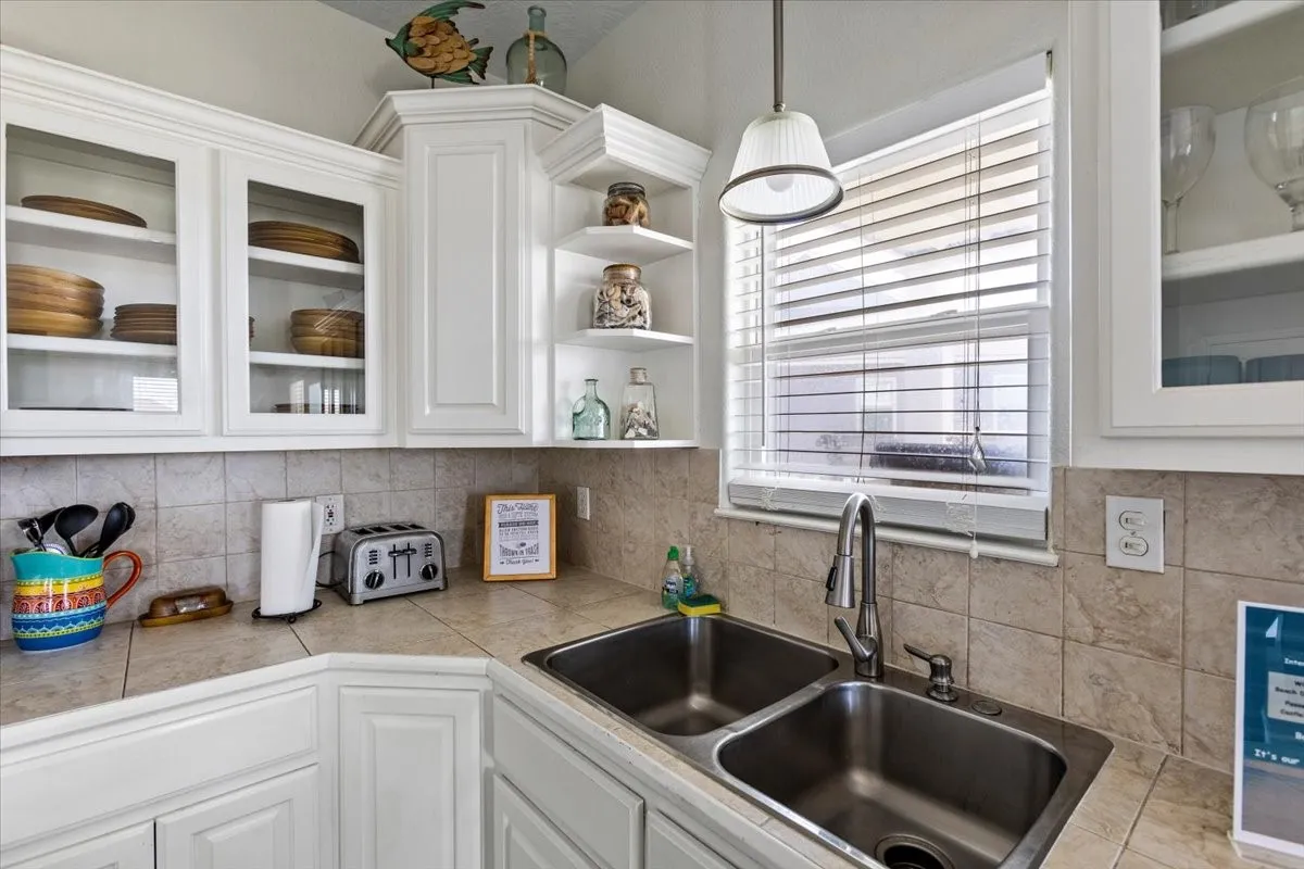 Kitchen with decorative backsplash, white cabinetry, and sink