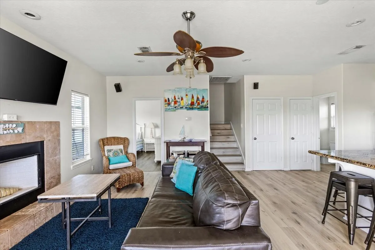 Living room with a tile fireplace, light wood-type flooring, and ceiling fan