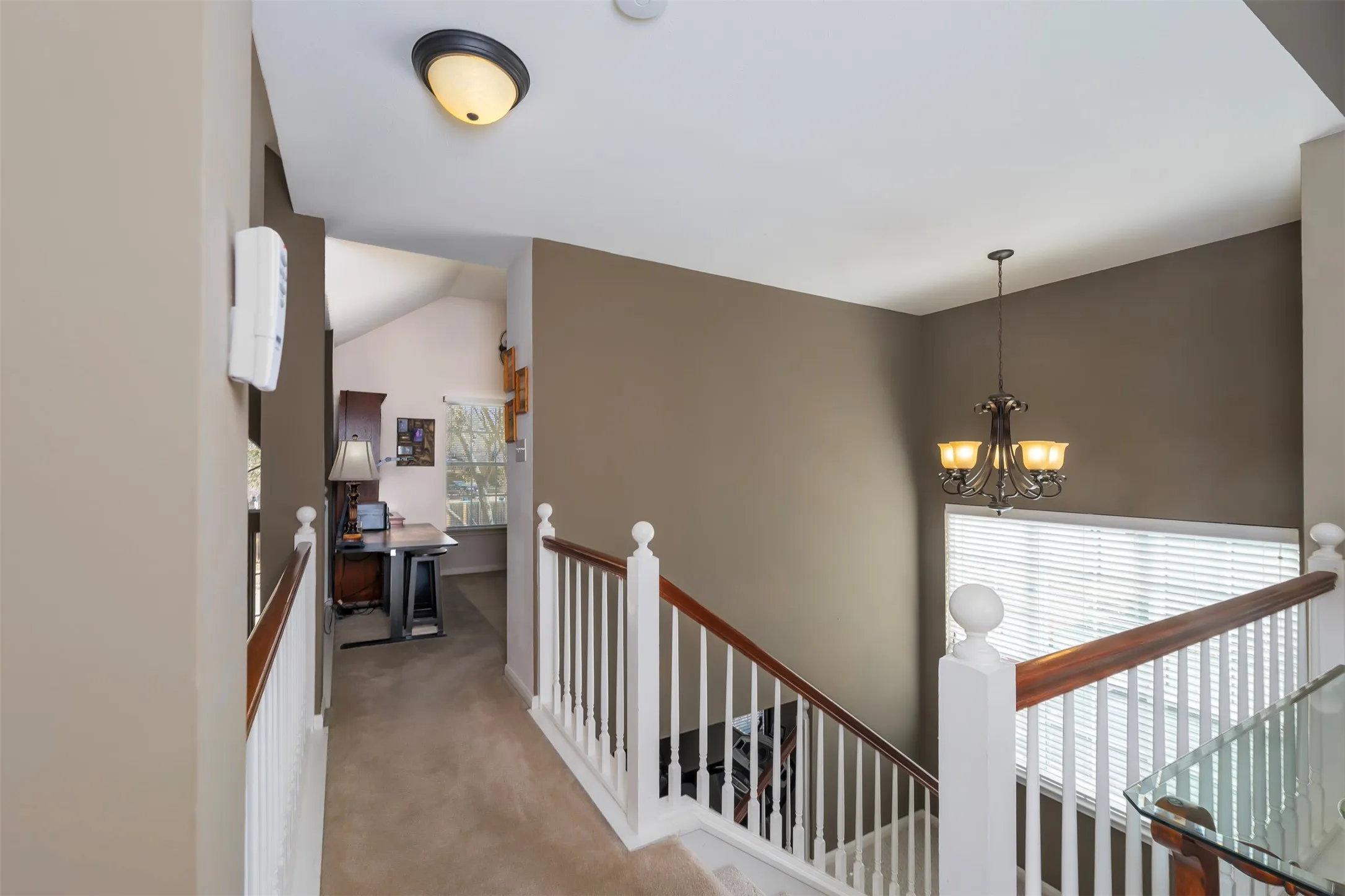 Corridor featuring an upstairs landing, lofted ceiling, light carpet, and hanging lights