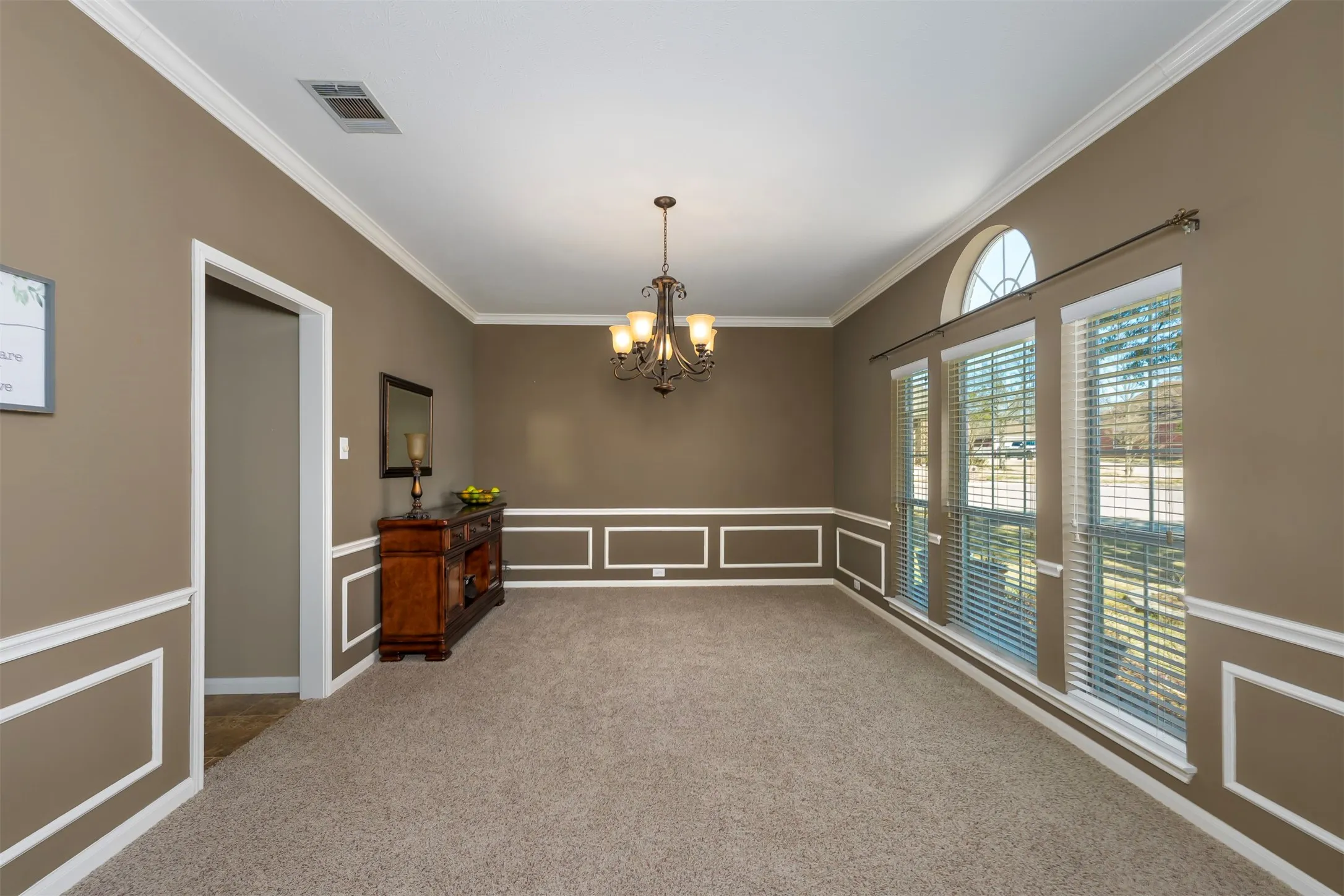 Unfurnished formal dining area featuring a decorative wall, hanging lights, ornamental molding, a wainscoted wall, and light carpet