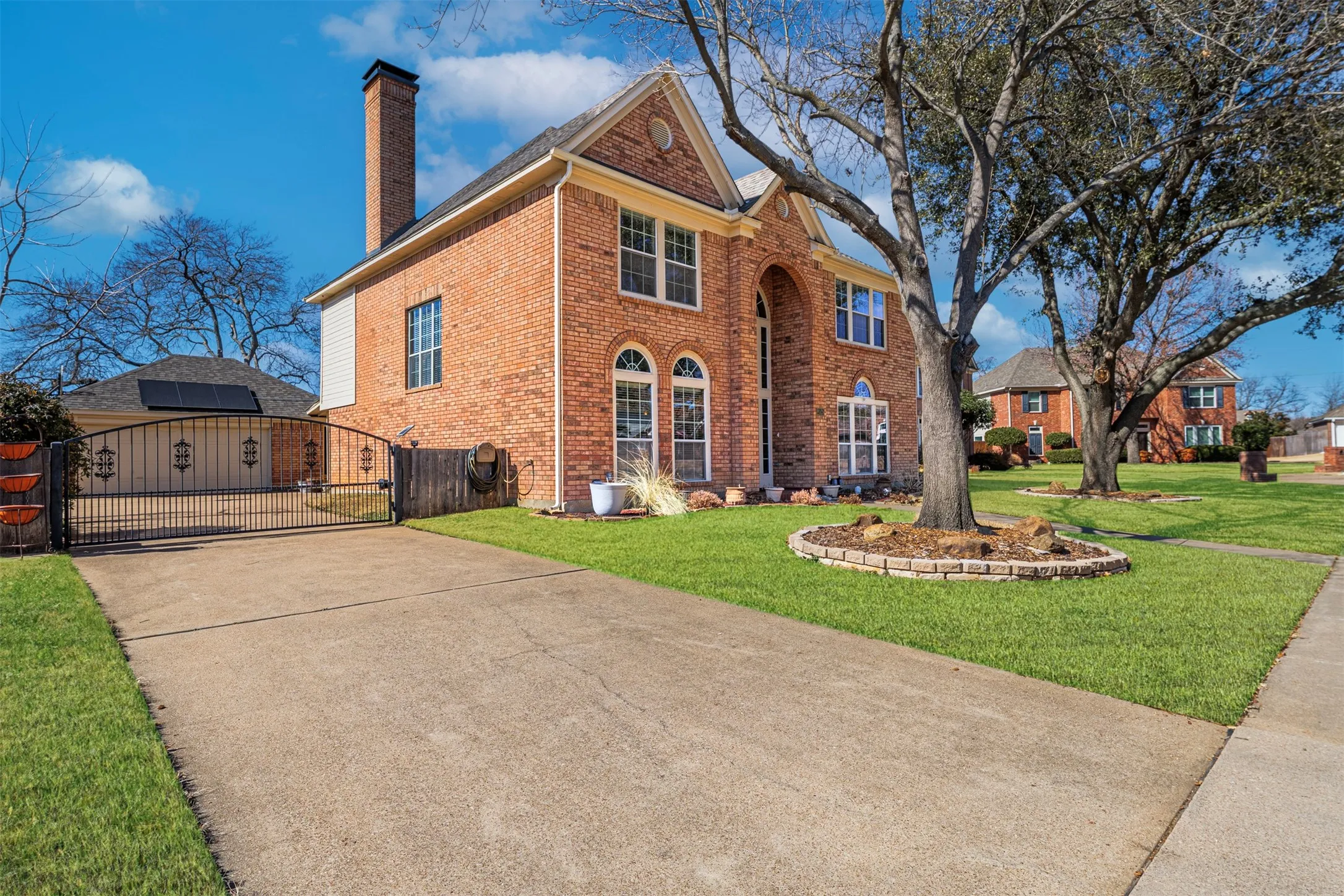 View of side of home featuring a gate, a chimney, brick siding, and concrete driveway