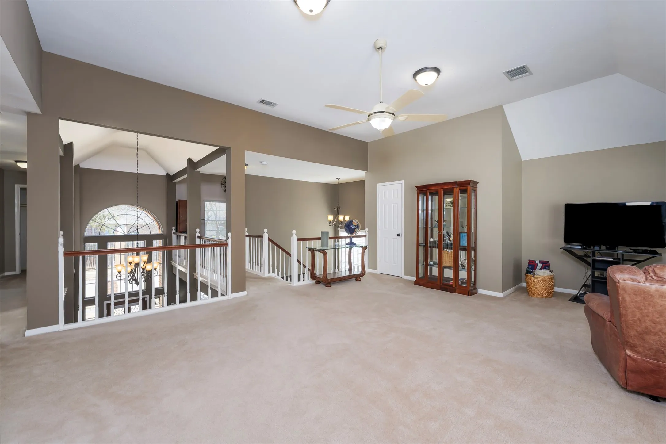 Living area with a chandelier, lofted ceiling, ceiling fan, light carpet, and an upstairs landing