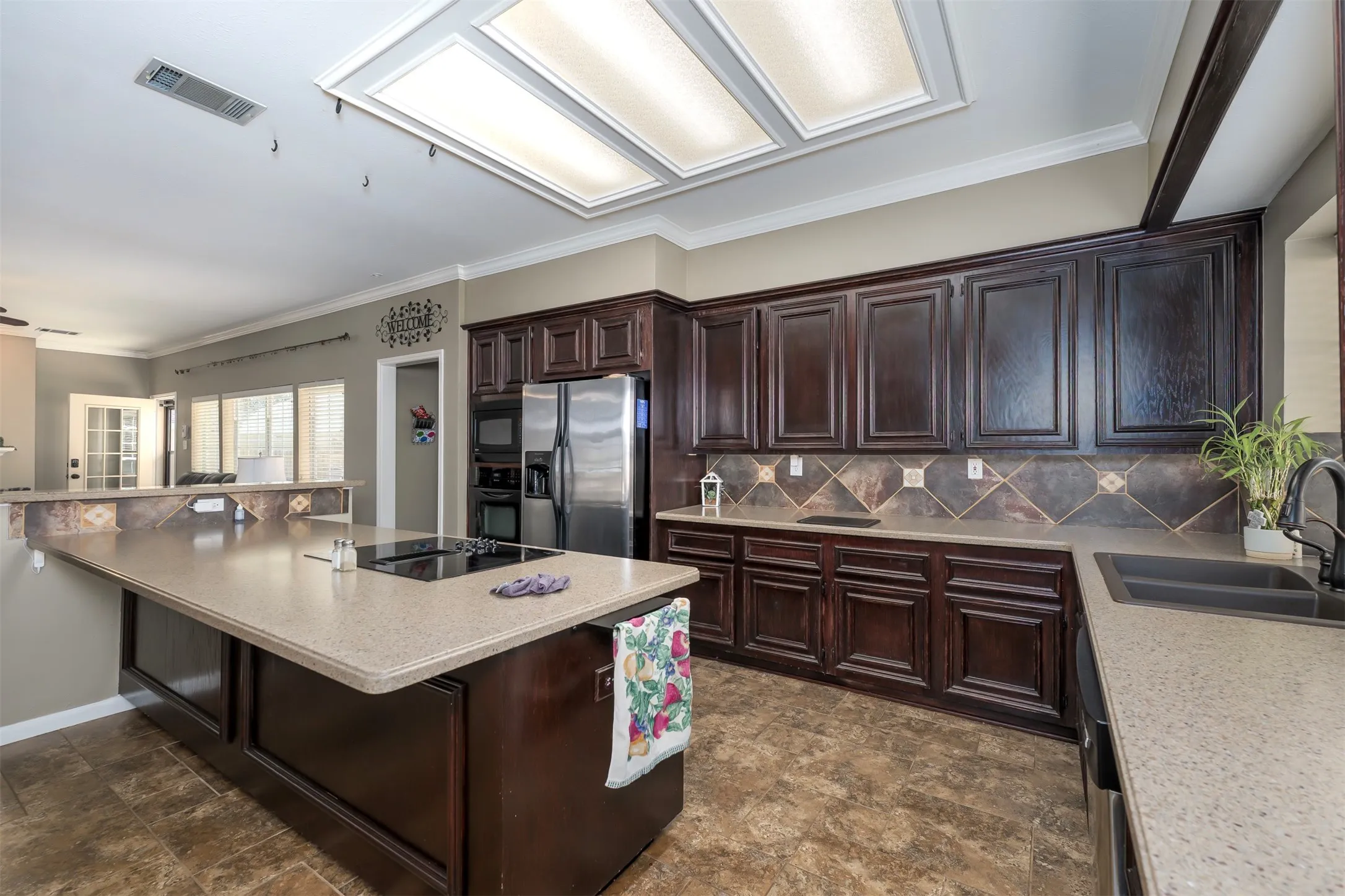 Kitchen featuring dark wood finish cabinetry, crown molding, stone finish flooring, black appliances, and light stone countertops