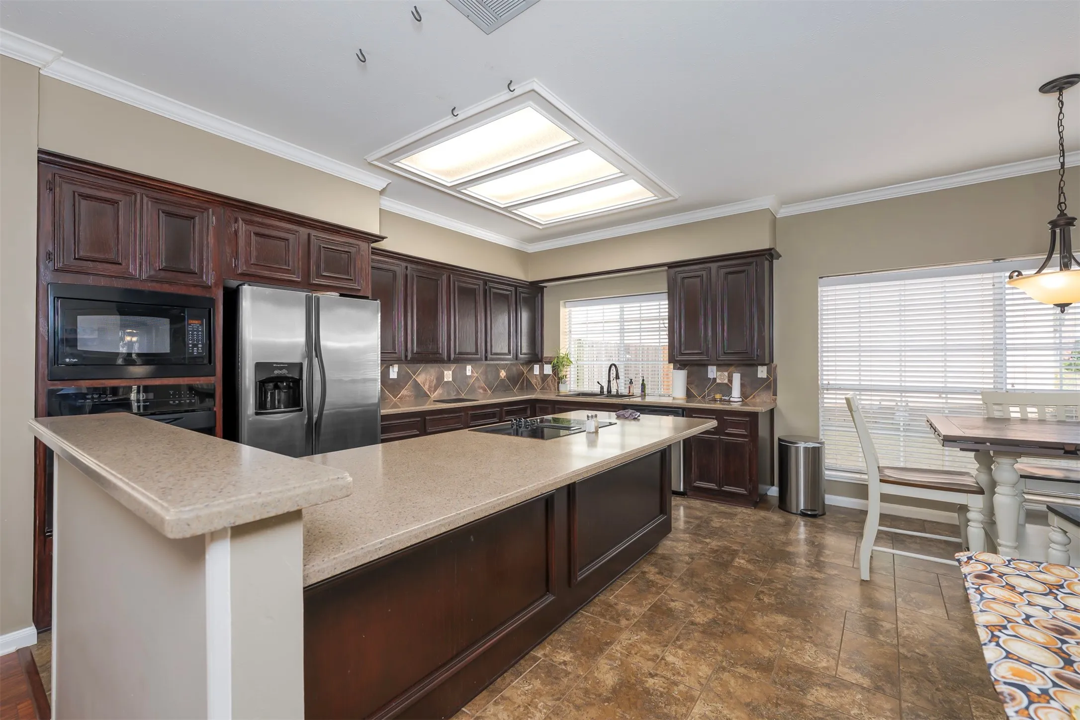 Kitchen featuring dark wood finish cabinets, black appliances, a center island, ornamental molding, and tasteful backsplash