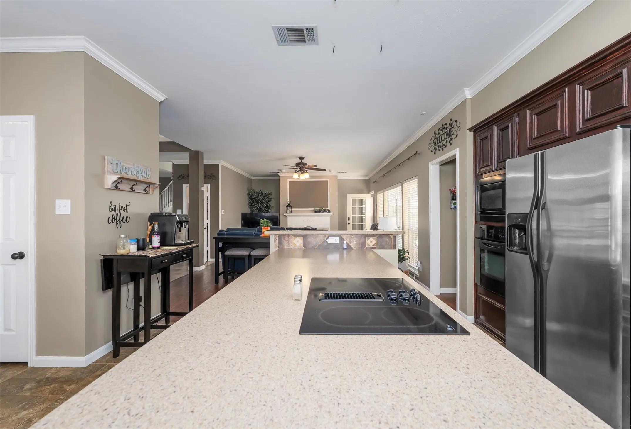 Kitchen with black appliances, crown molding, open floor plan, dark wood finish cabinets, and light stone counters