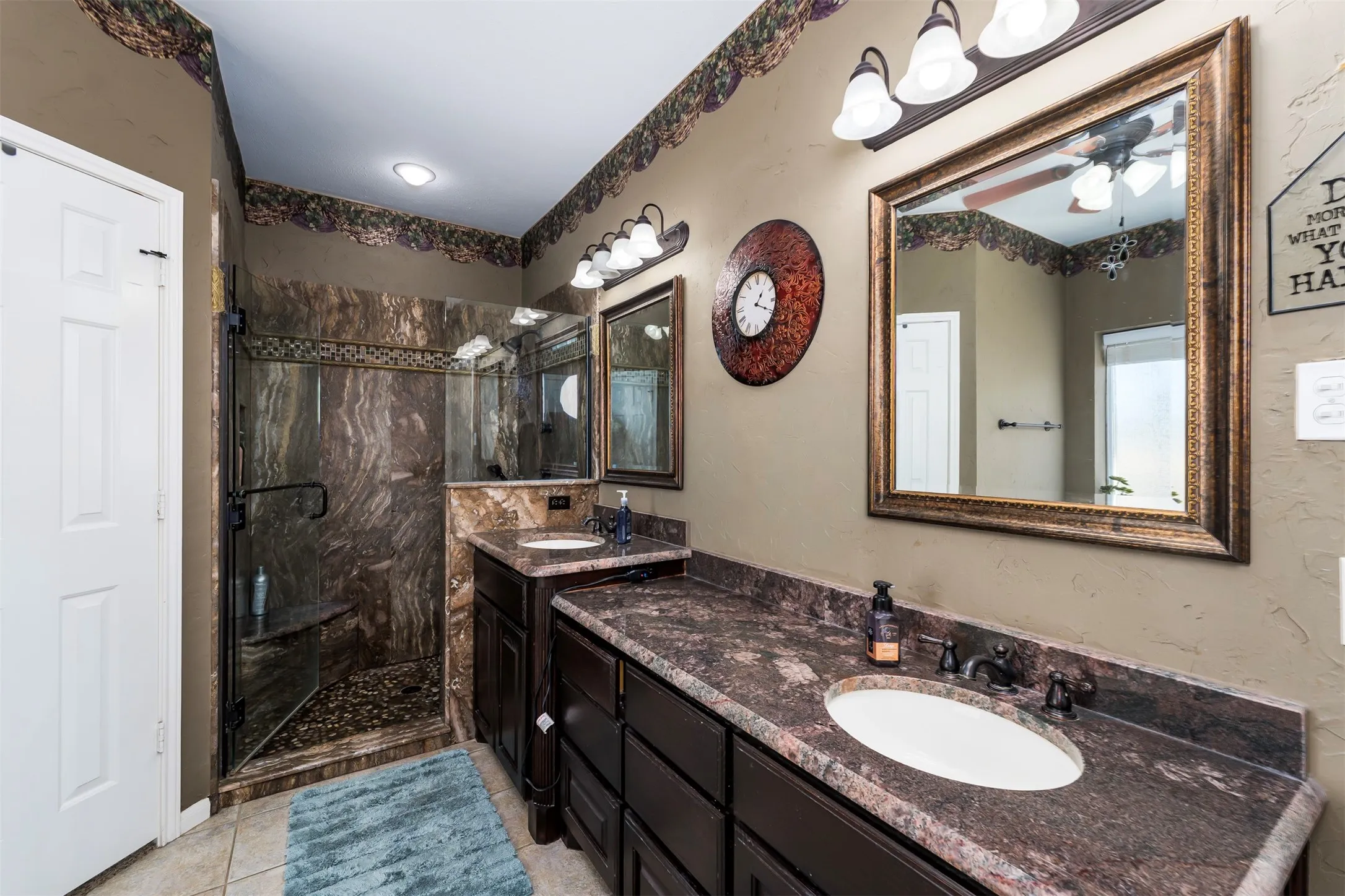 Bathroom with double vanity, a marble finish shower, ceiling fan, and light tile patterned flooring