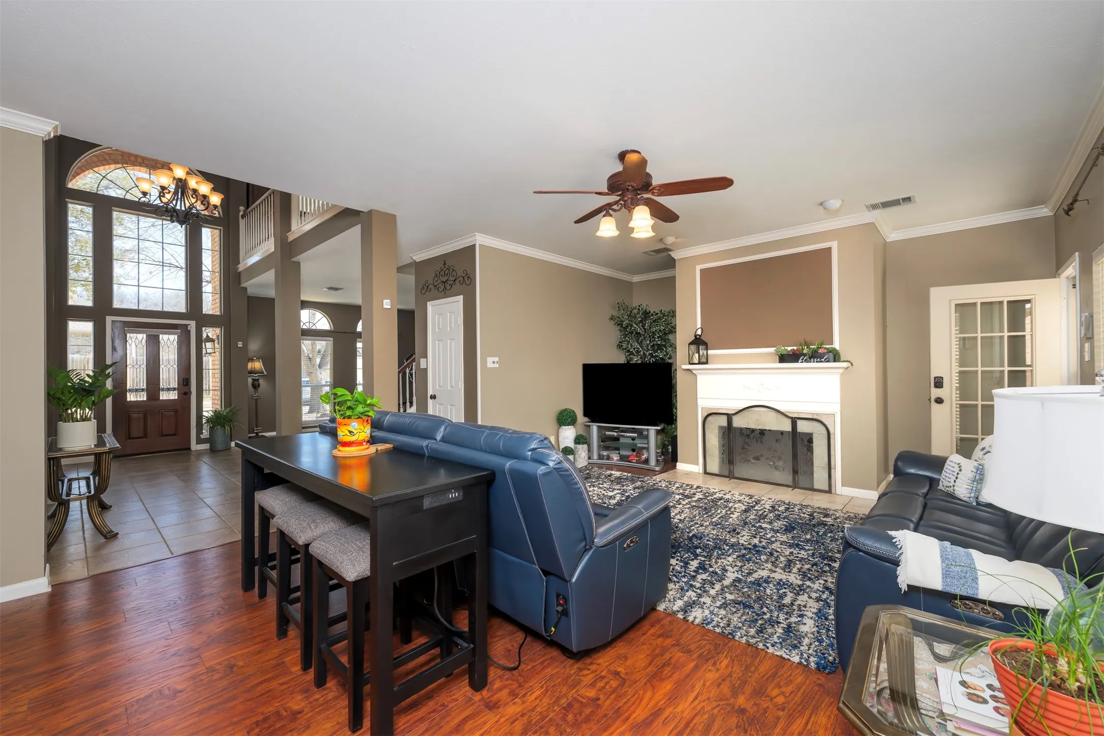 Living area featuring wood finished floors, a fireplace, a ceiling fan, crown molding, and suspended lighting
