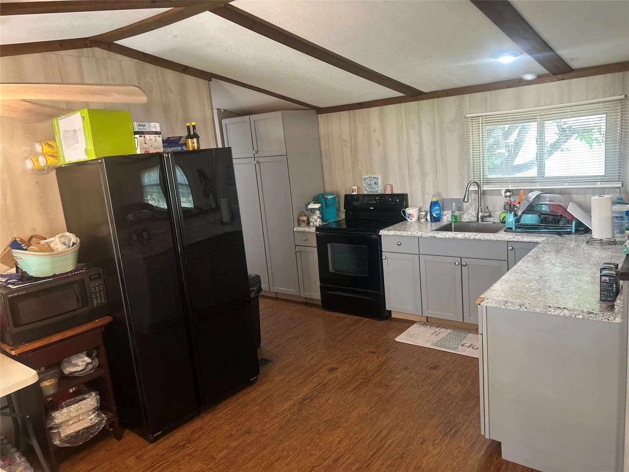 Kitchen featuring black appliances, gray cabinetry, light countertops, dark wood-style flooring, and wooden walls