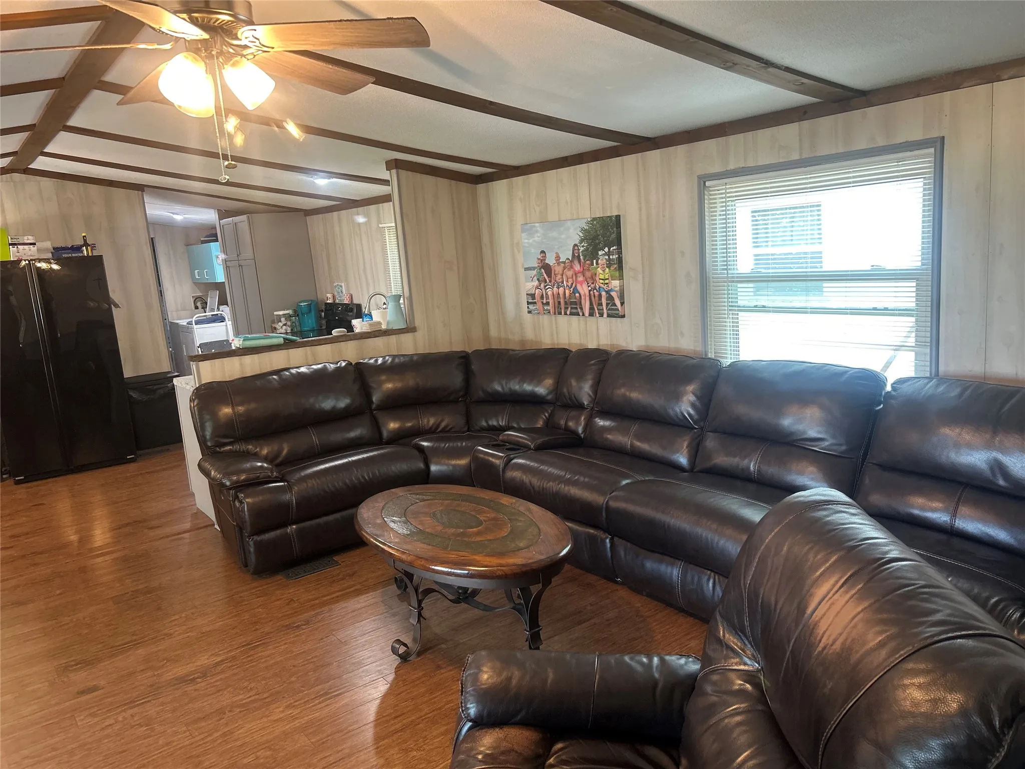 Living room with wood finished floors, beamed ceiling, wooden walls, and a ceiling fan