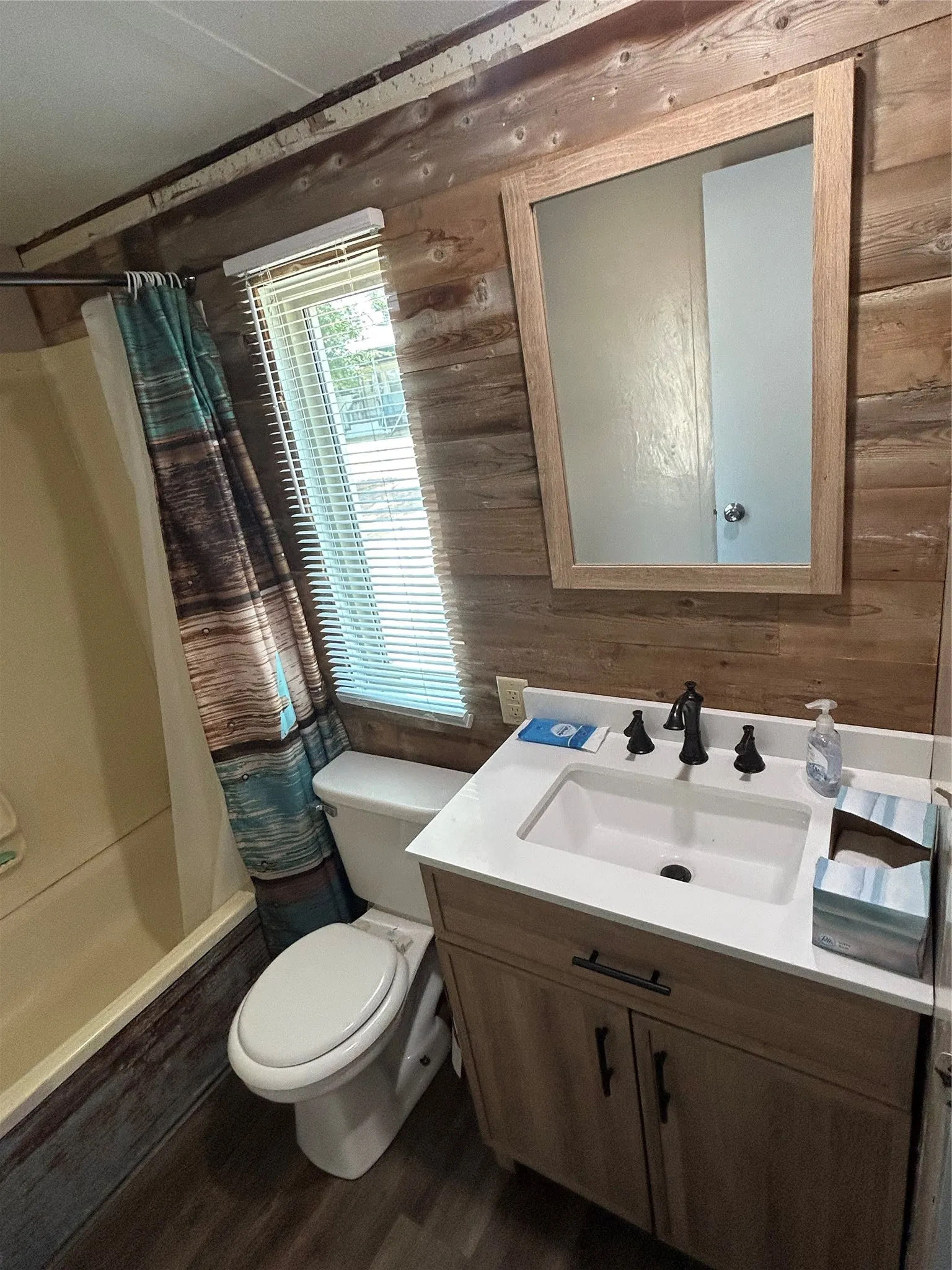 Full bath featuring wooden walls, vanity, wood finished floors, and shower / bathtub combination with curtain