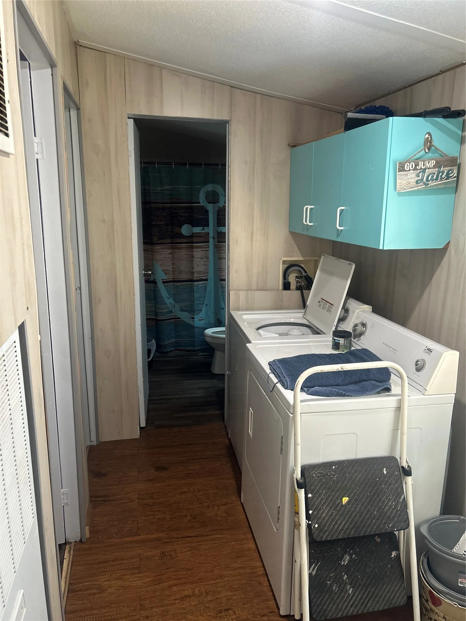 Laundry room with washer and clothes dryer, cabinet space, dark wood finished floors, and wood walls